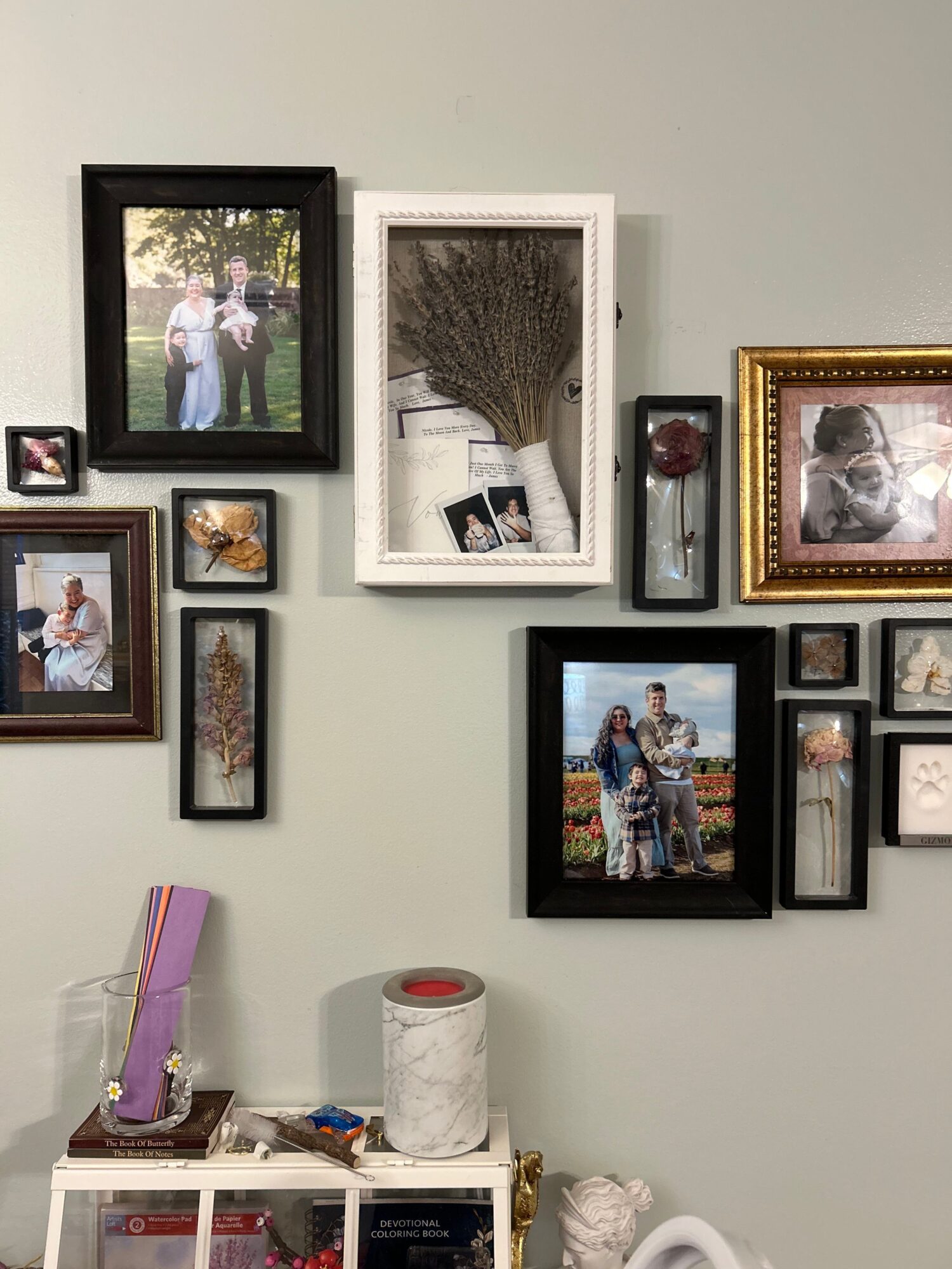 Wall with multiple framed photographs and artwork, some in black and white, arranged in a collage style.