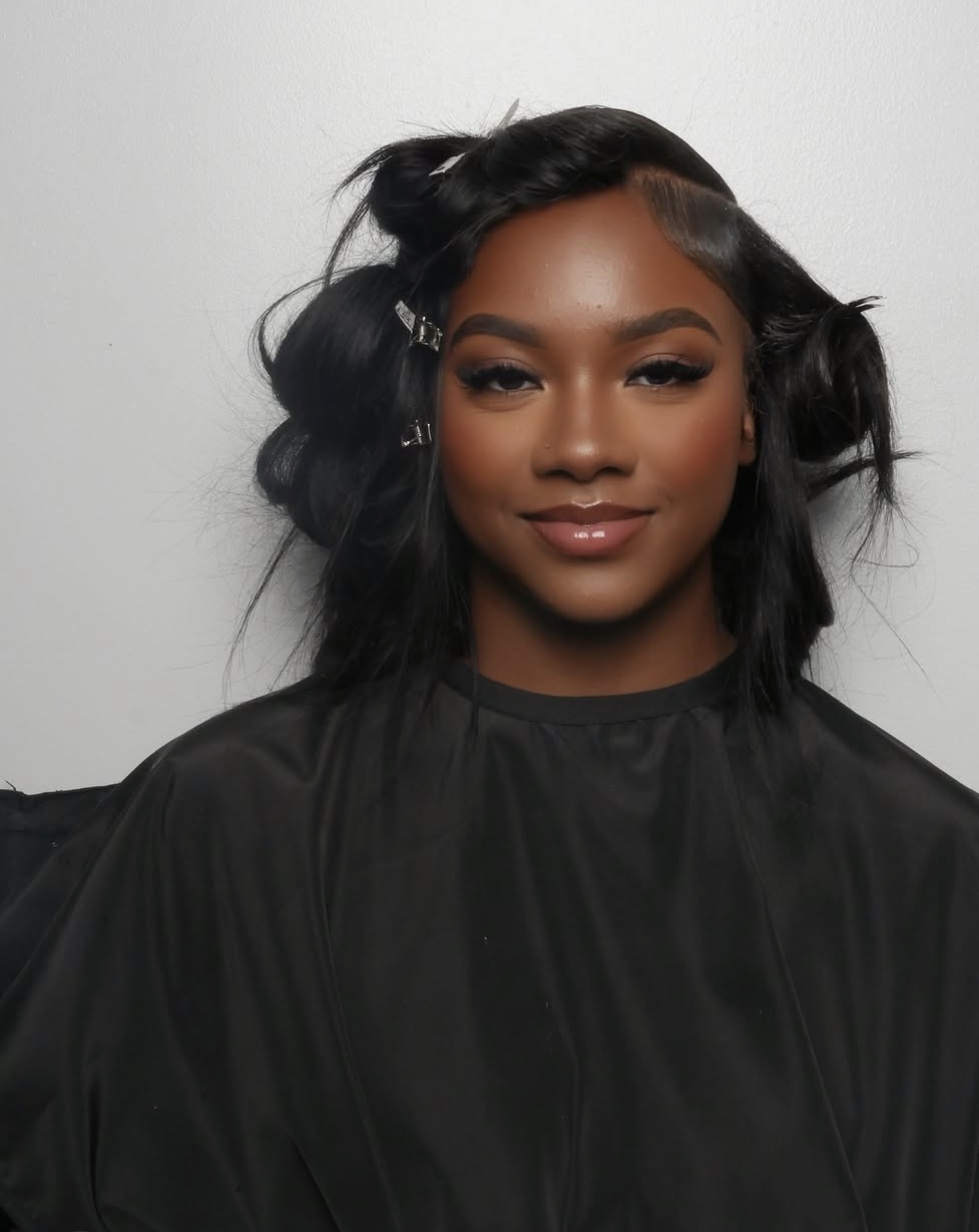 Portrait of a woman with styled black hair, wearing a black top, smiling softly against a plain background.