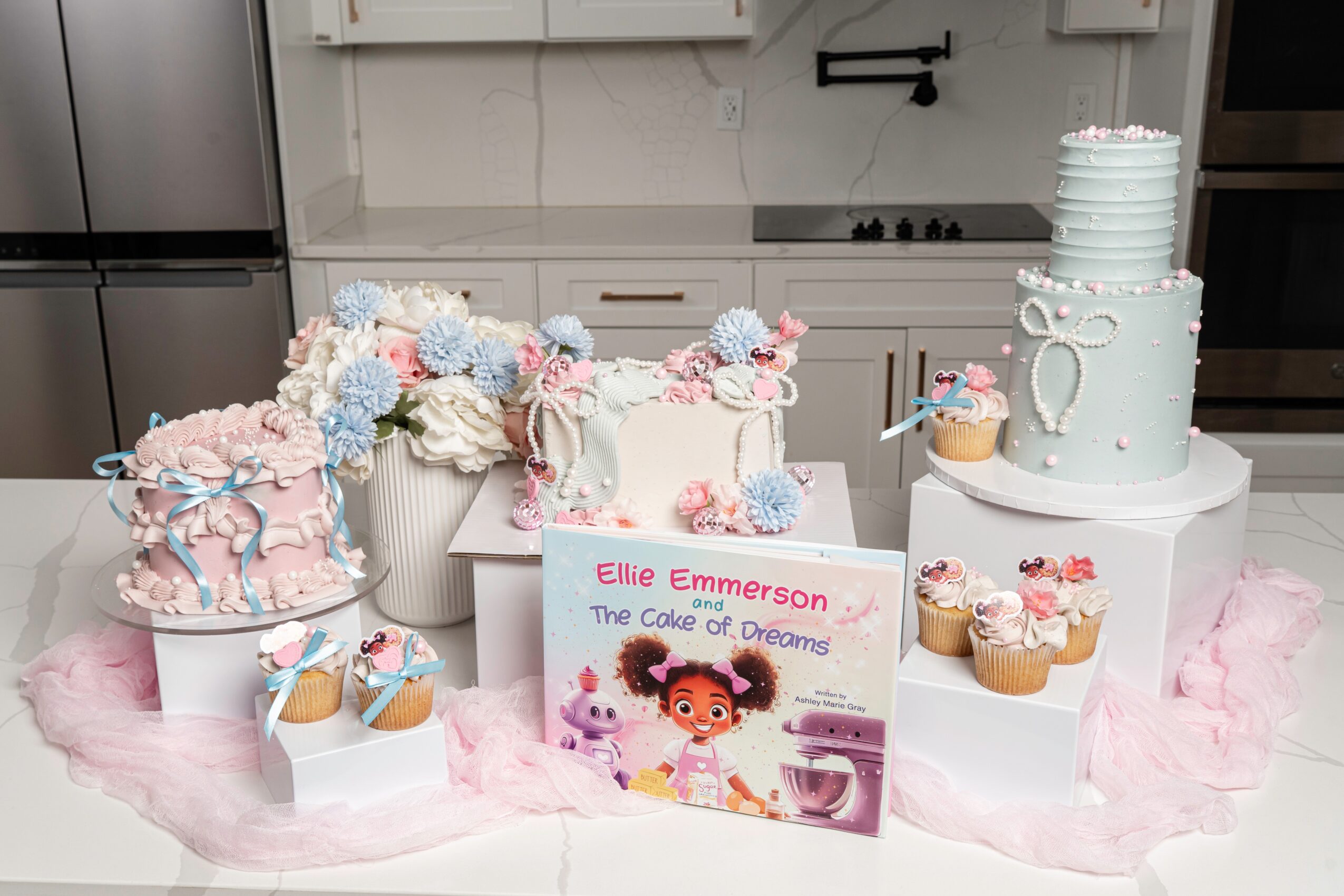 Birthday cake, cupcakes, and a card on a table with pink tulle, in a kitchen setting.
