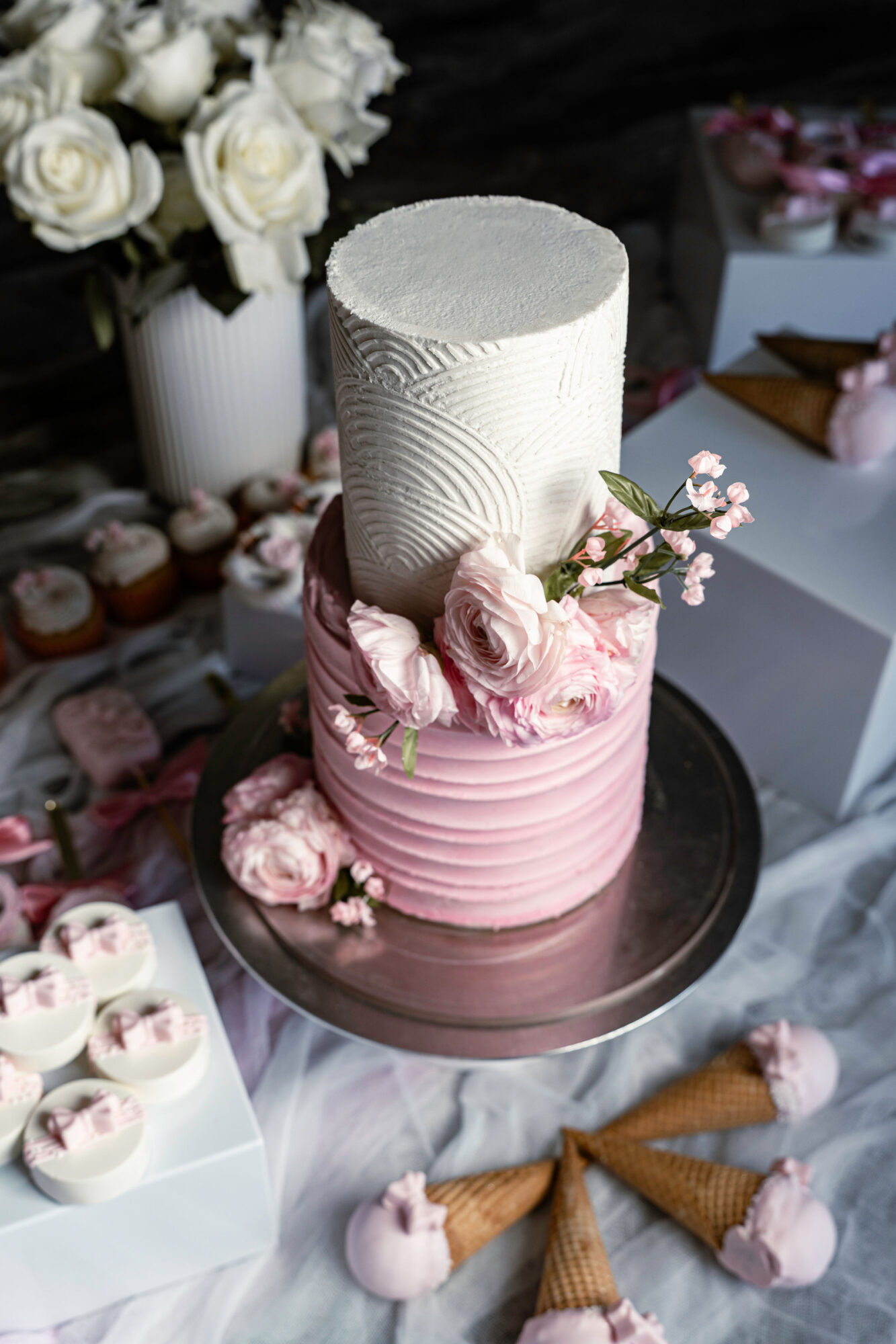 Two-tiered cake with white top and pink bottom, decorated with pink roses and small flowers, on a black tray.