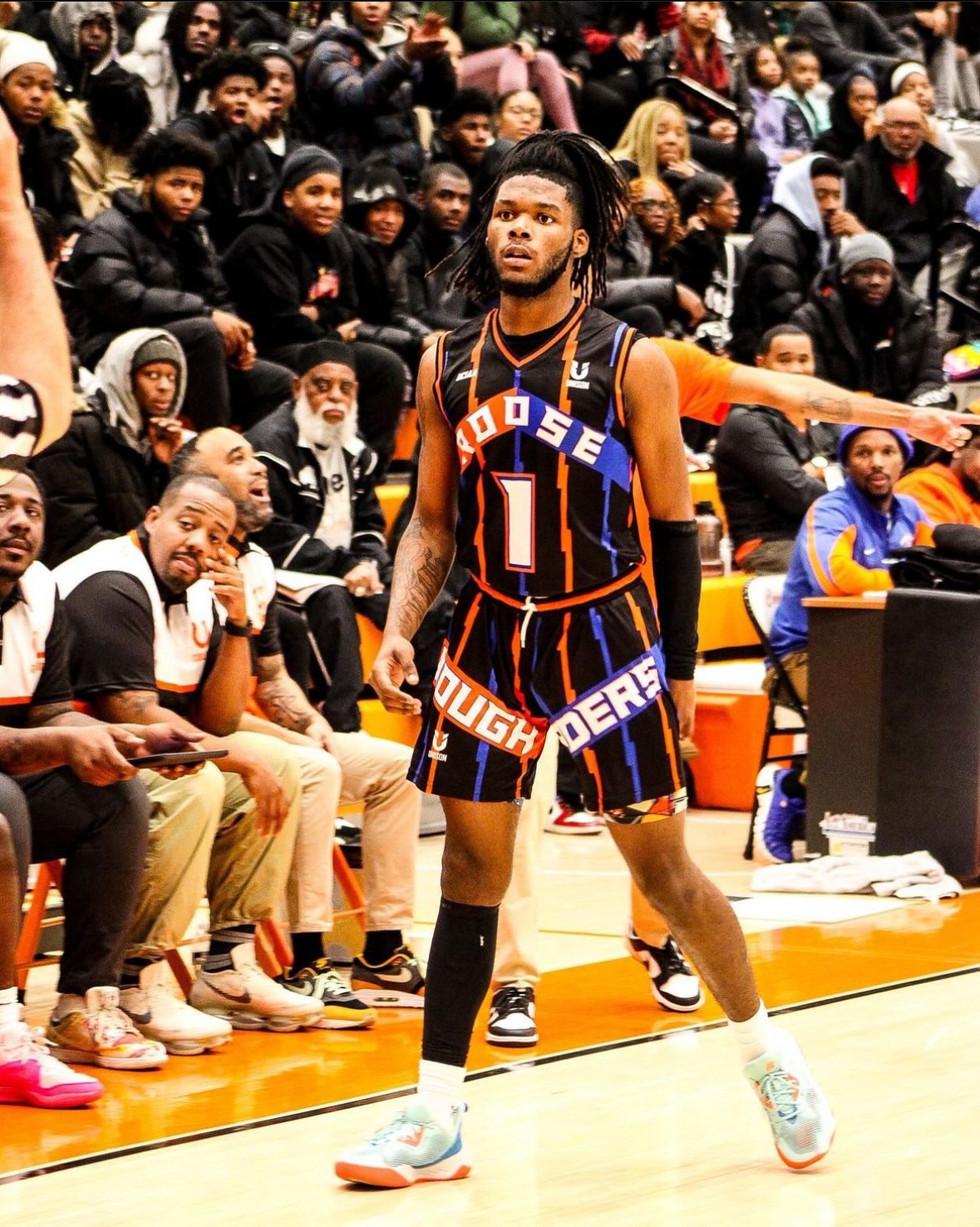 Basketball player in uniform standing on court with spectators in background.