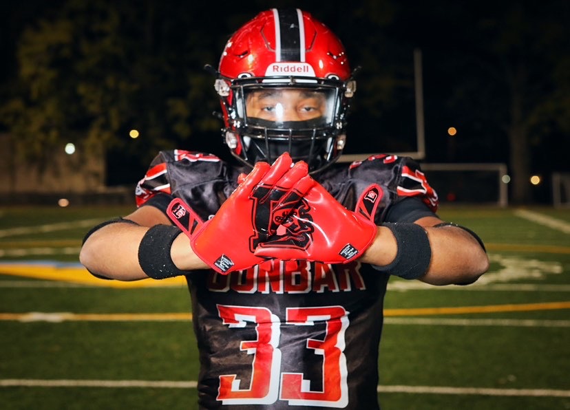 Football player in black and red uniform with helmet, gloves, and number 33, standing on field at night