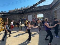 People dancing outdoors in front of a stone building with a clear blue sky.