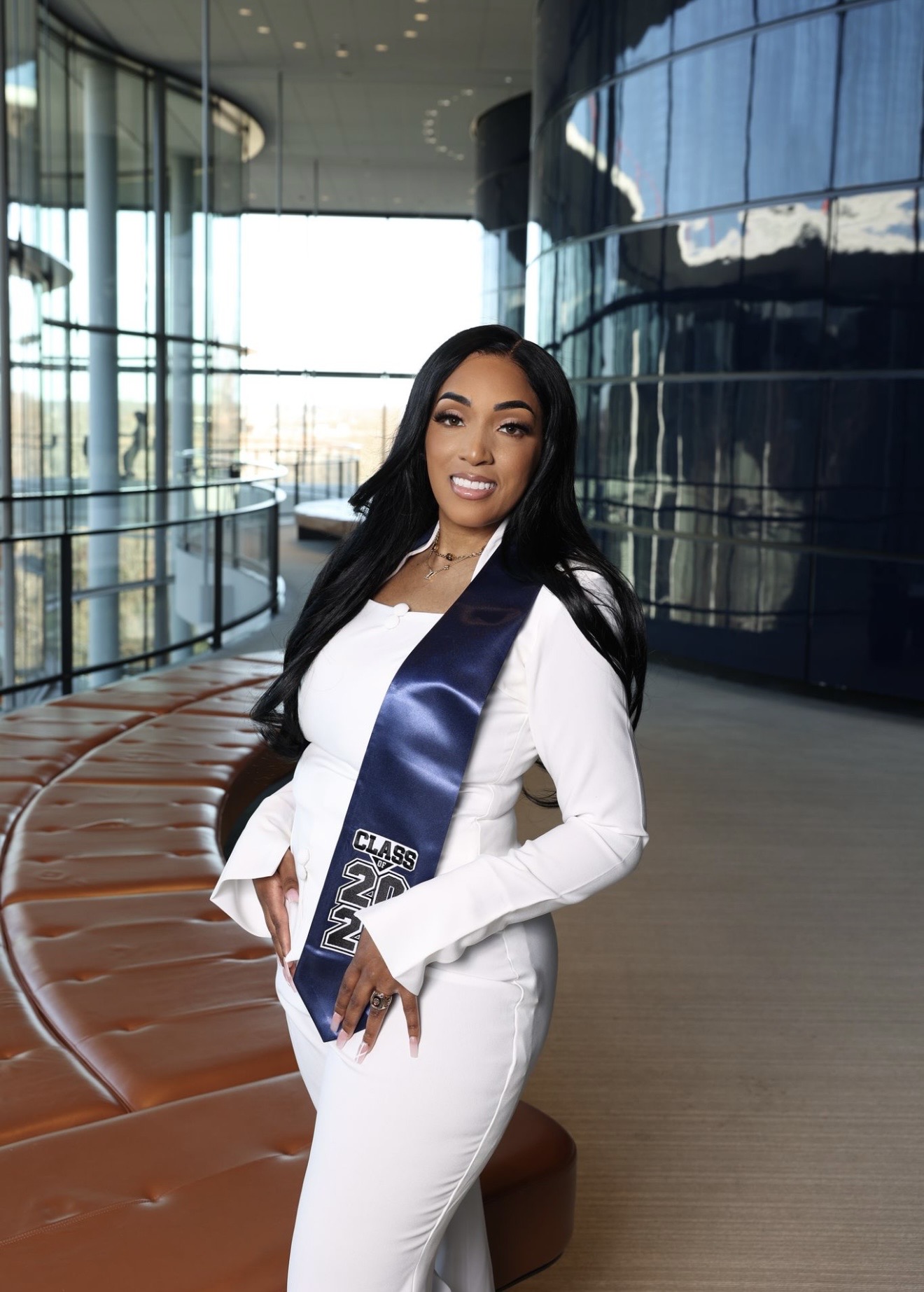 Woman in white outfit standing indoors with glass walls and modern architecture, smiling at camera.