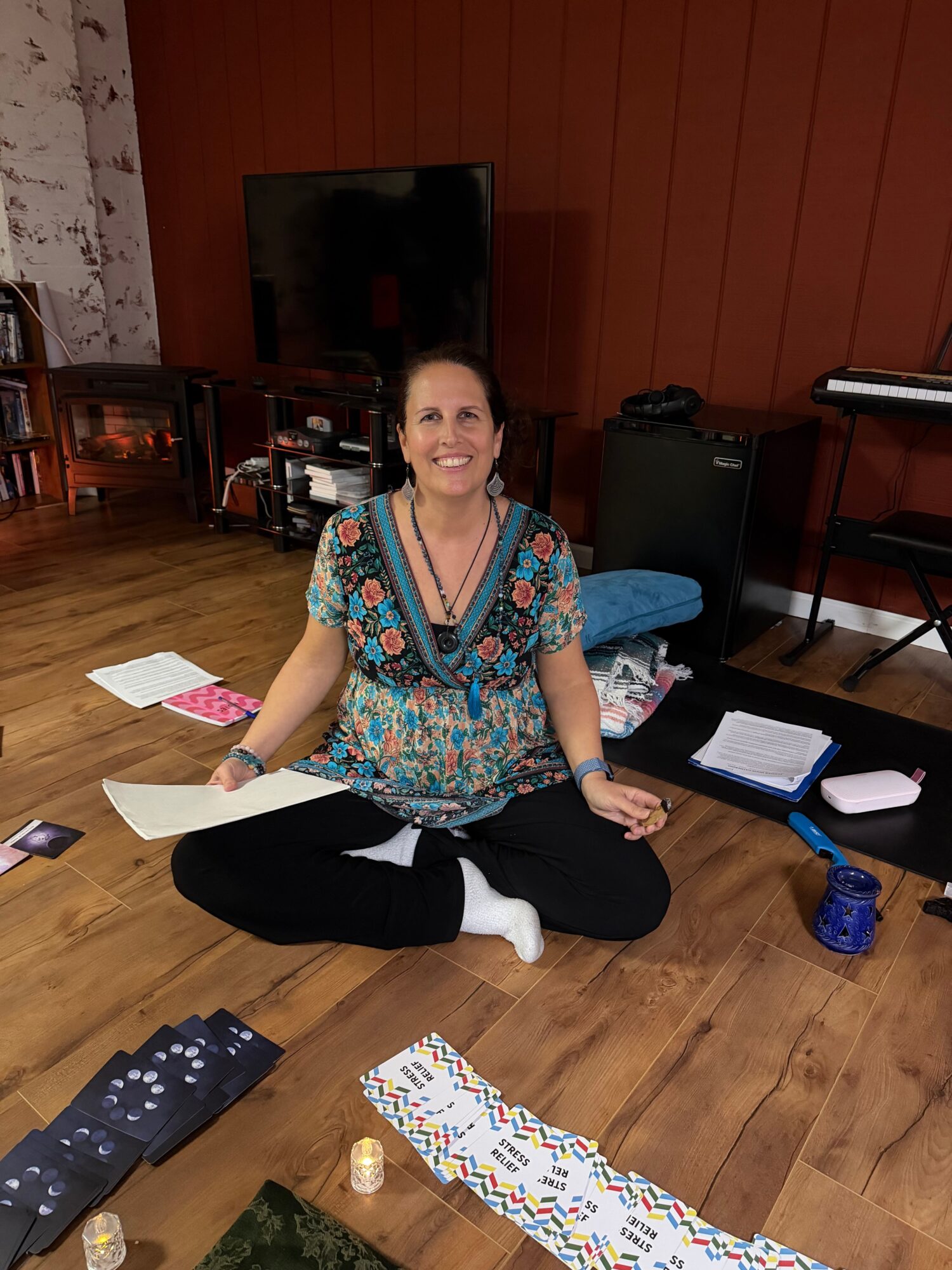 Woman sitting on the floor with papers, a water bottle, and a phone, smiling at the camera.