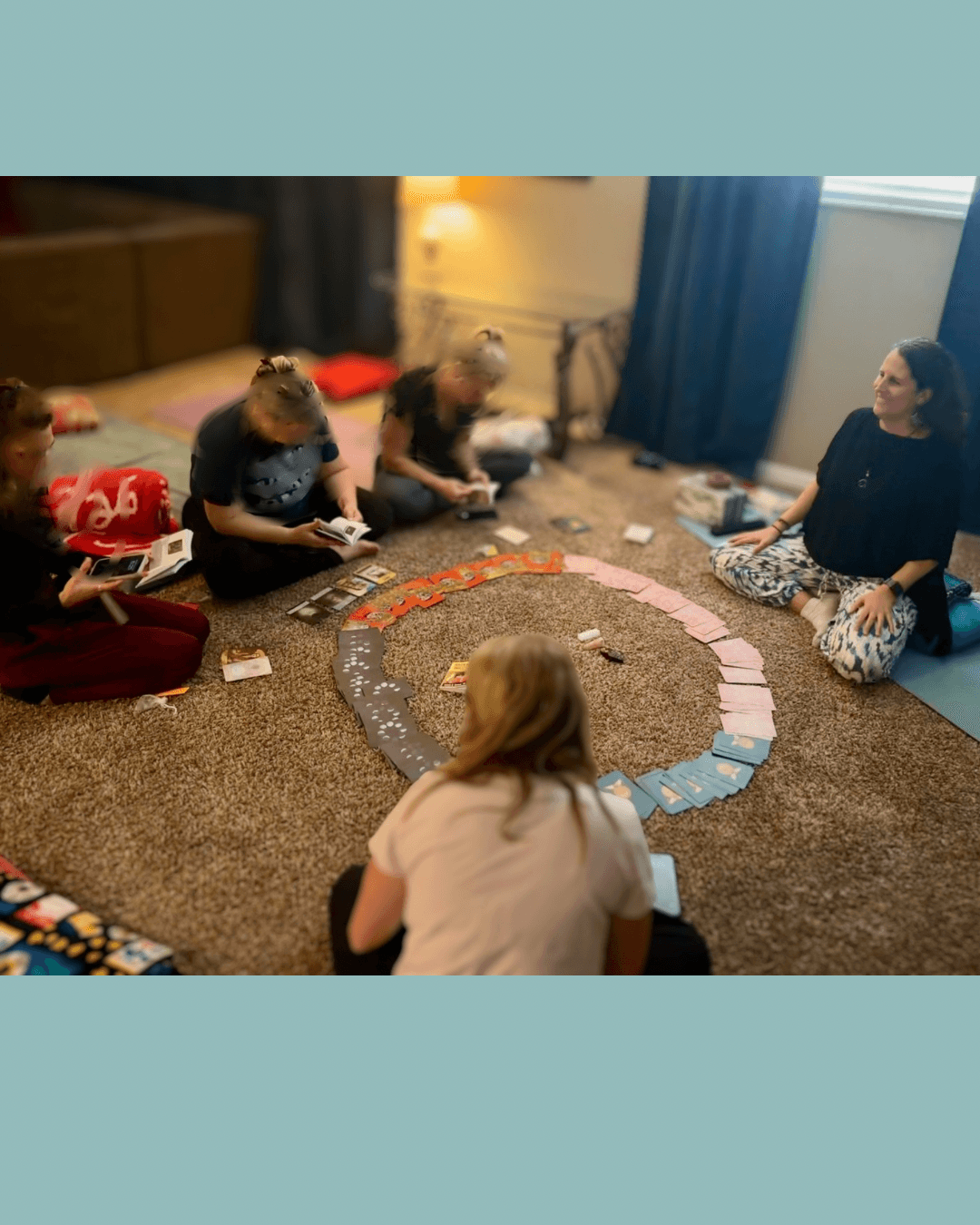 Group of people sitting on carpeted floor, playing a game with colorful tiles arranged in a circle, in a cozy room.