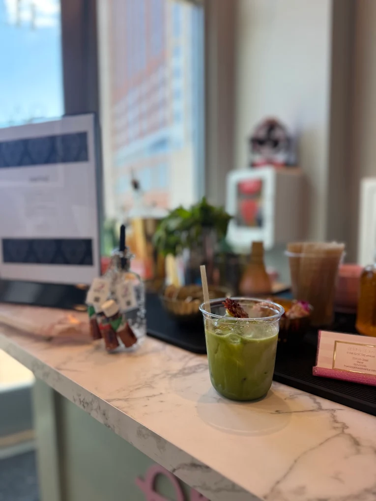 Green beverage in a glass on a marble countertop with blurred background of a window and indoor objects.