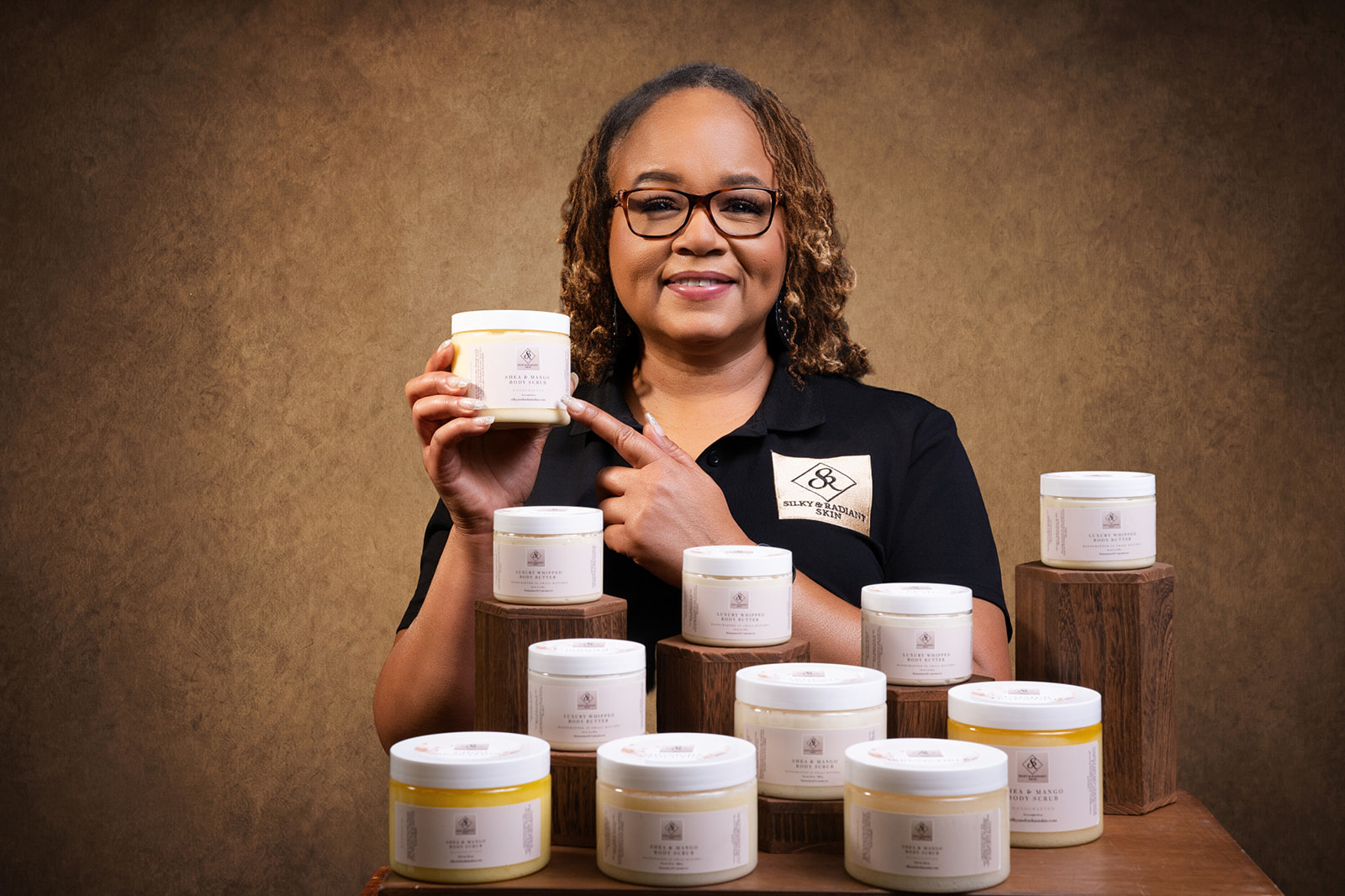Smiling woman with glasses holding a container, surrounded by other containers on a table, against a brown background.