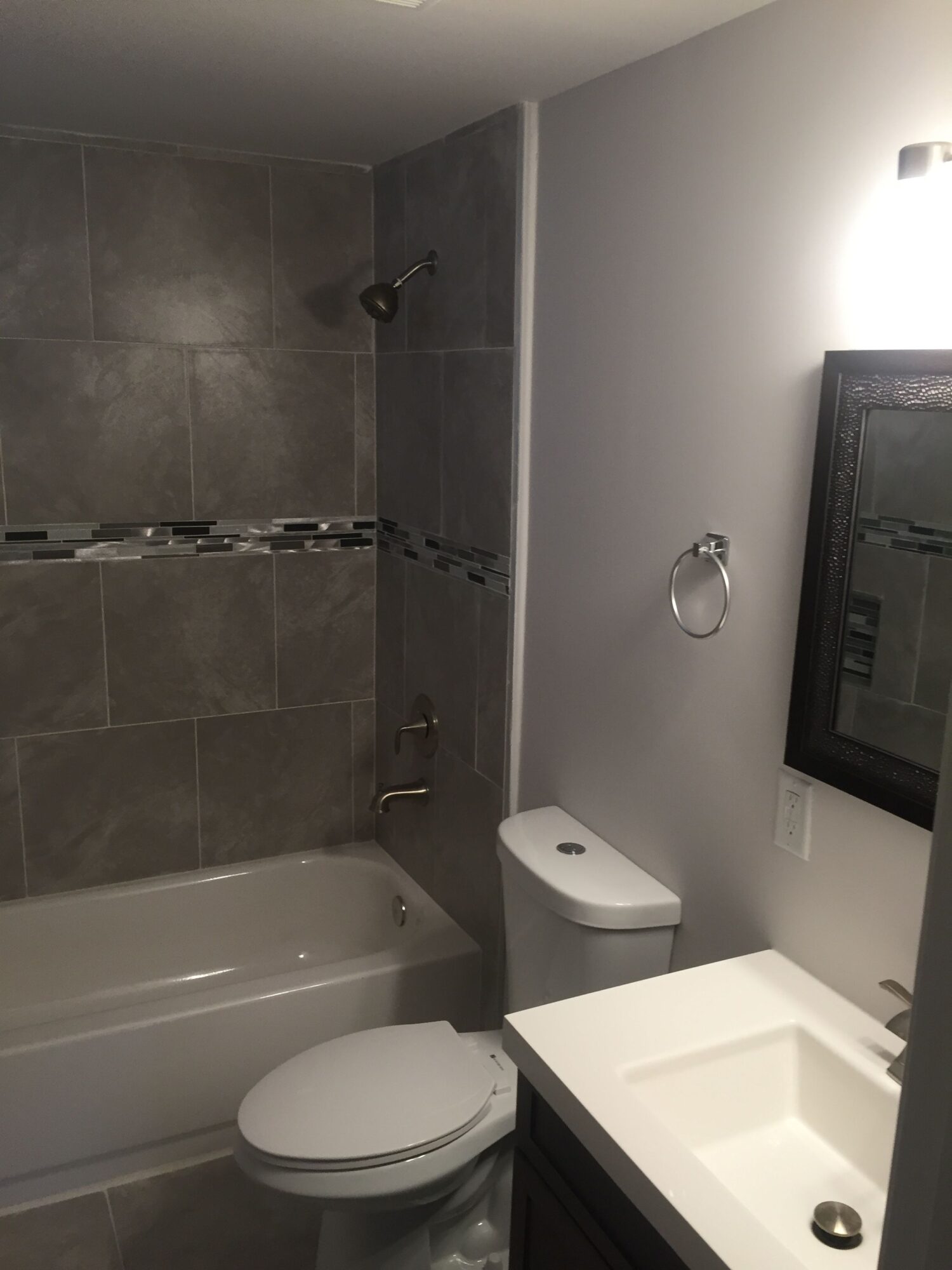 Bathroom with toilet, sink, mirror, and tiled wall, viewed from the side, with a window above the toilet.