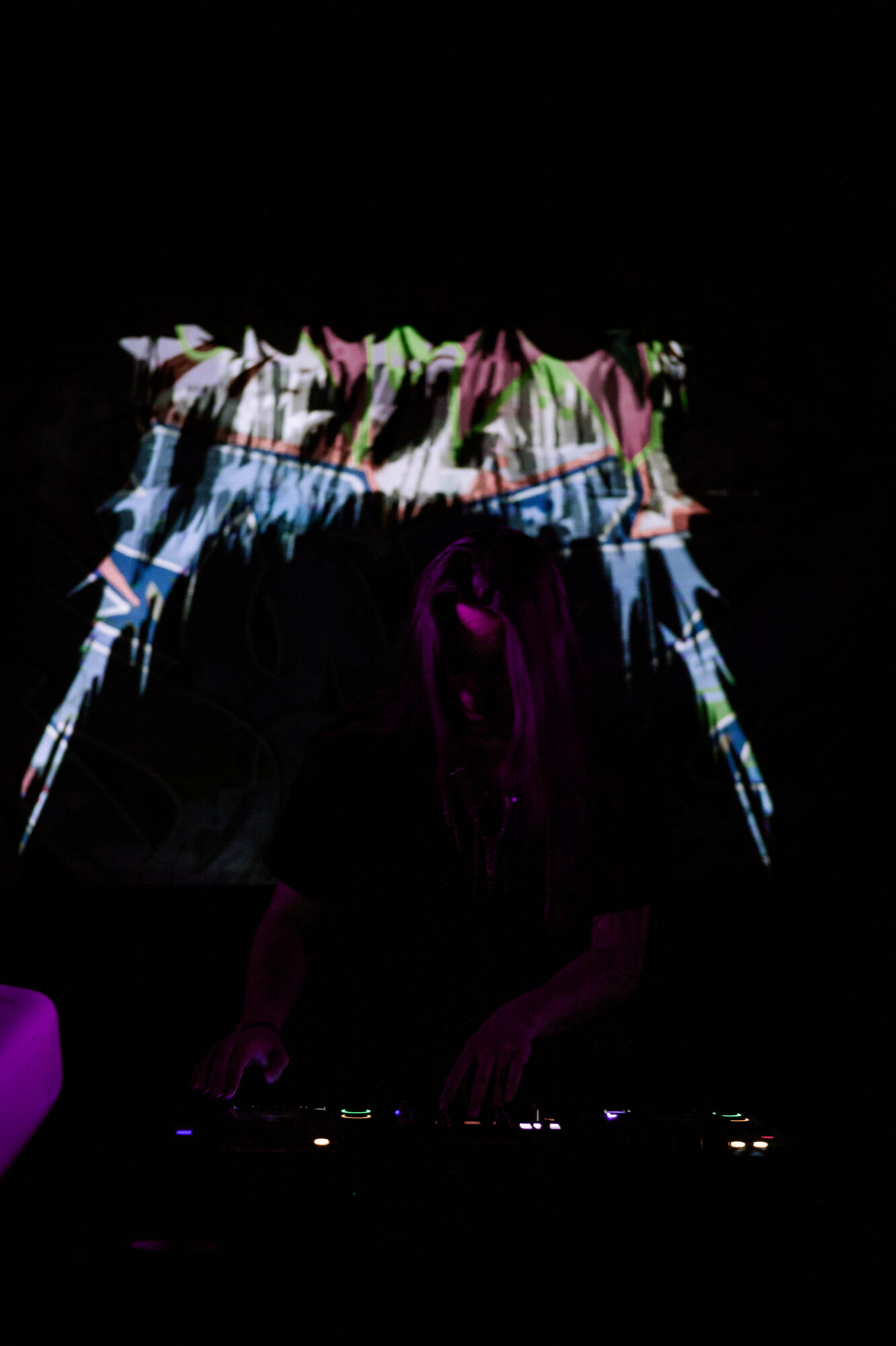Person standing in front of a colorful, abstract light display with dark background.
