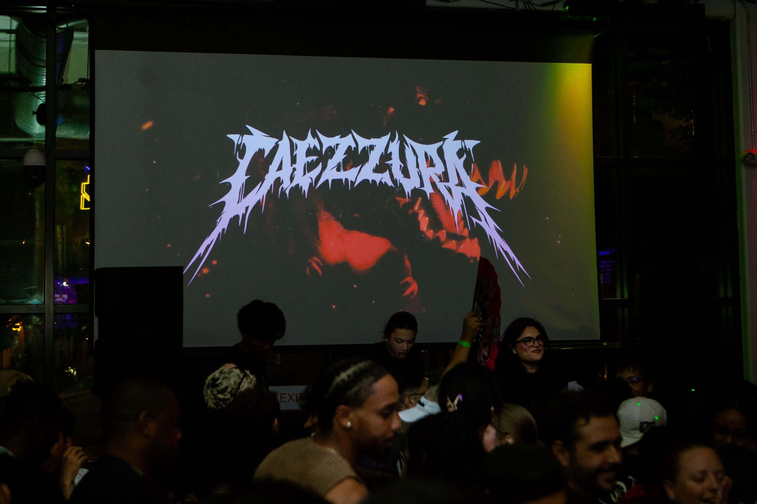 People sitting in front of a large screen displaying a logo with stylized text and a dark background.