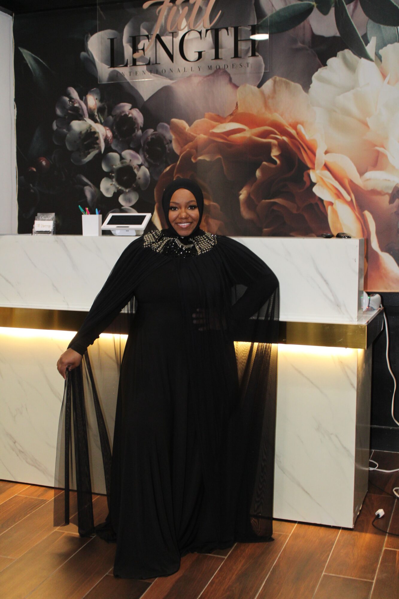 Woman in black dress standing in front of a white marble counter with a floral background.