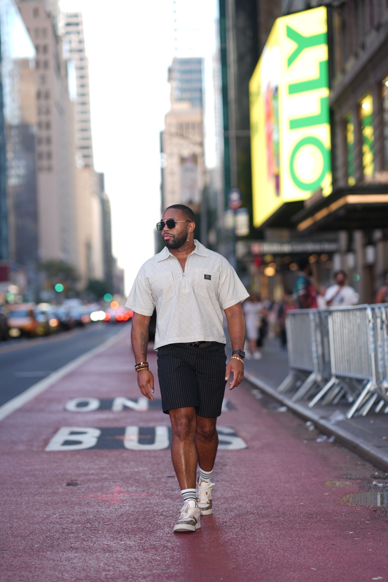 Man walking on city street with tall buildings and a large green and yellow sign in the background.