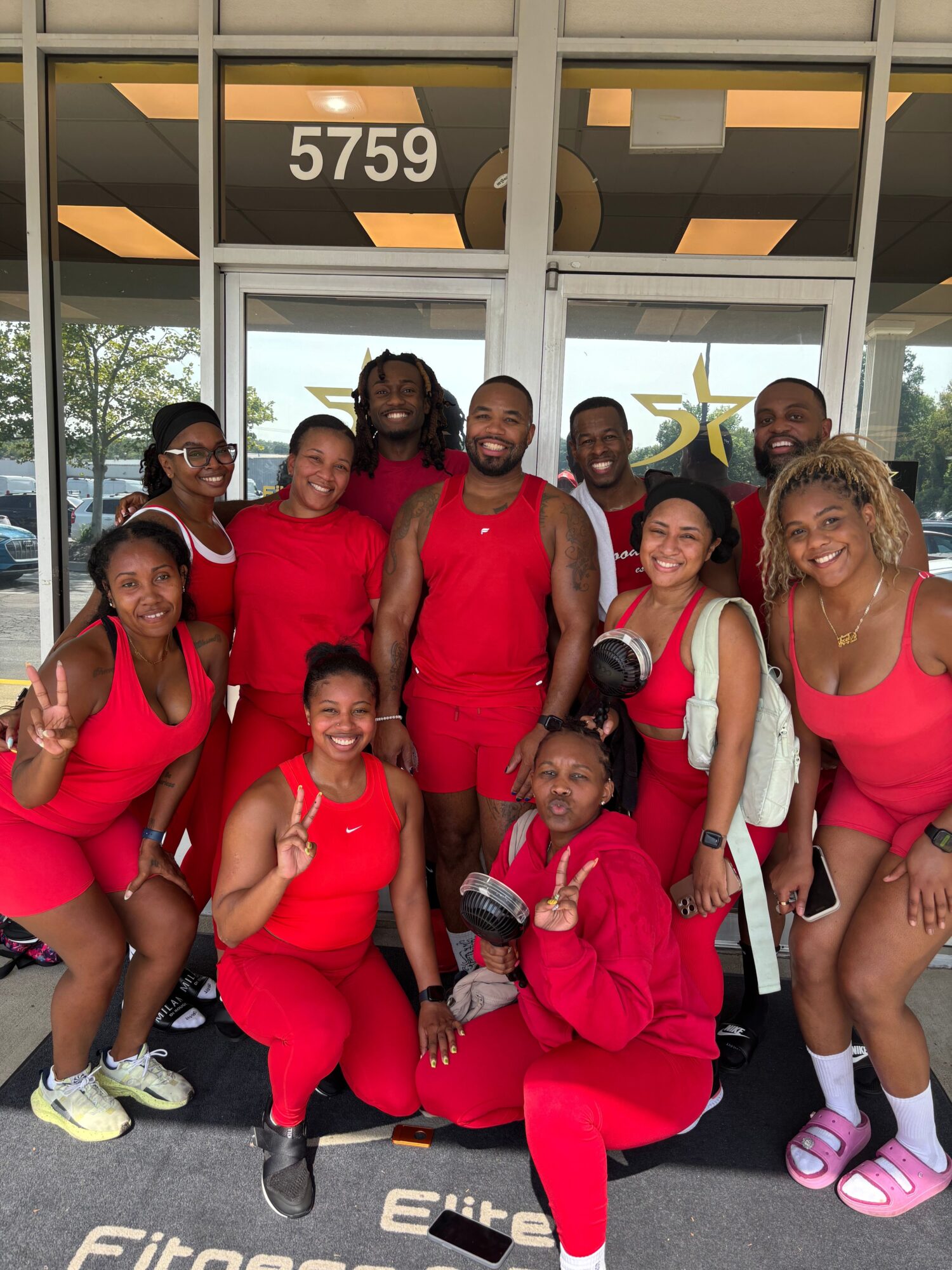Group of people in red outfits sitting and standing outside near a building, smiling and making peace signs.