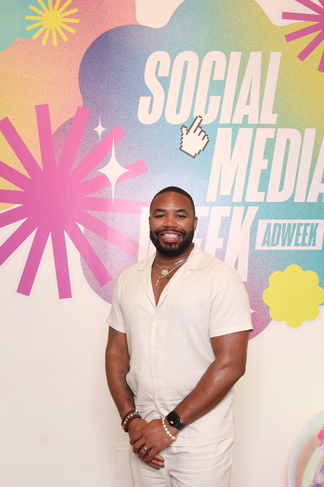 Smiling man in light-colored shirt standing in front of a colorful social media-themed backdrop with text and graphics.