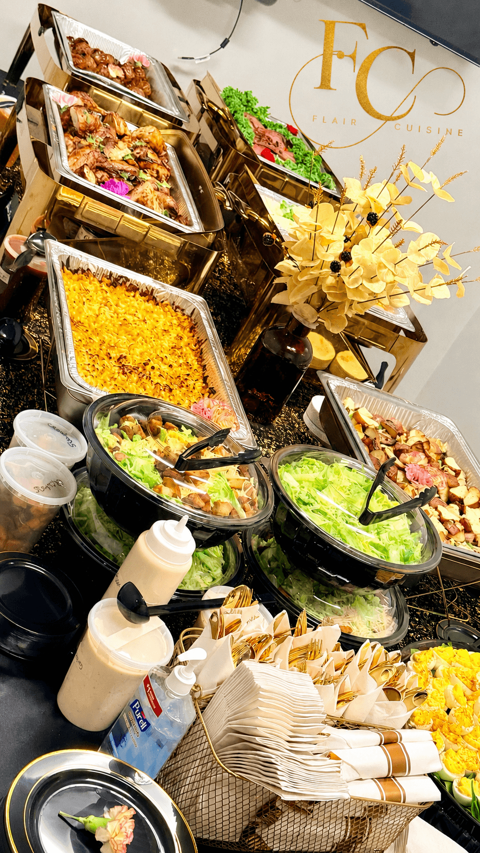 Salad bowls, condiments, and food containers on a buffet table with a decorative flower arrangement in the background.