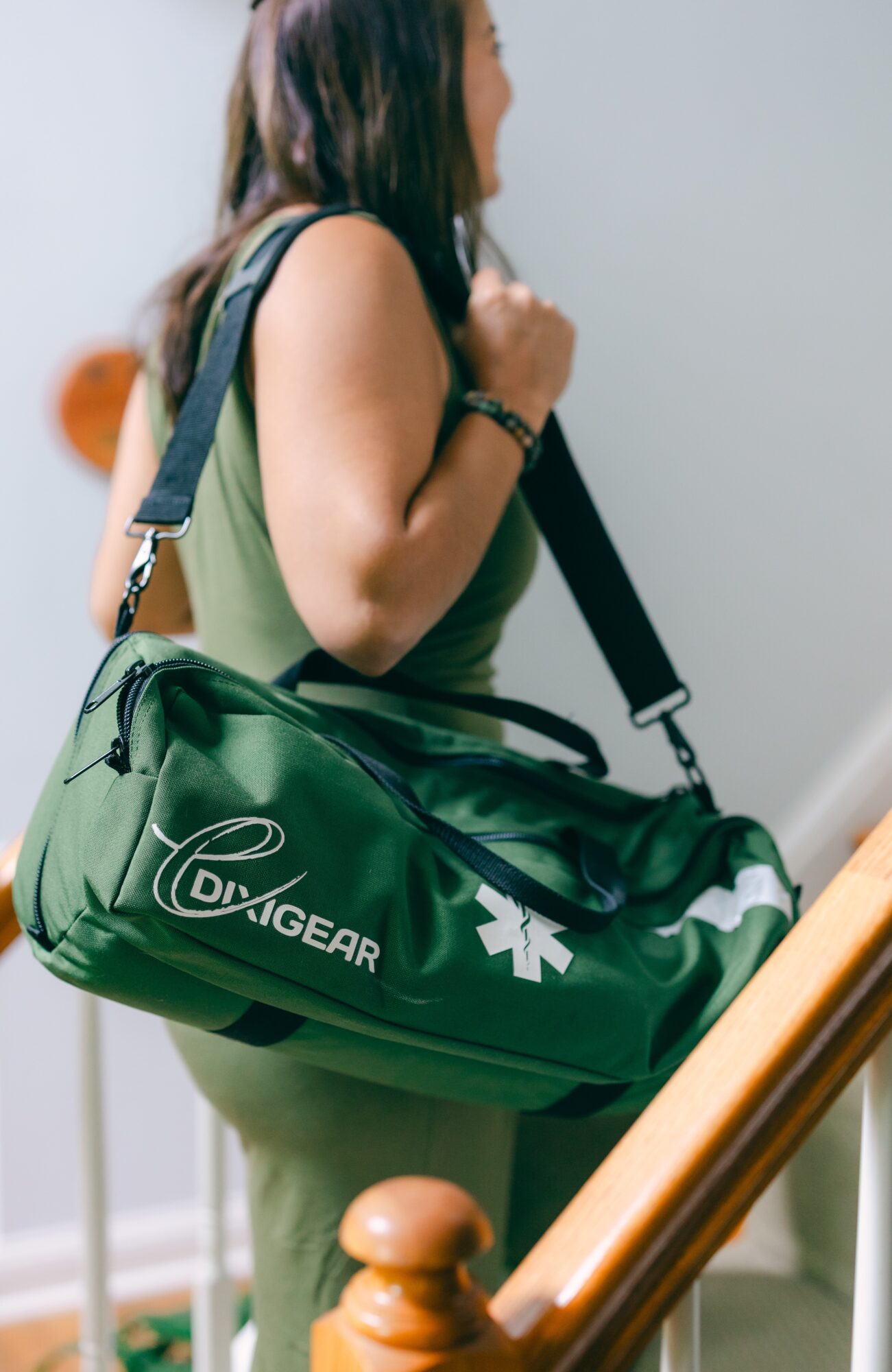 Side view of a person carrying a green medical bag with a shoulder strap, standing near a staircase.