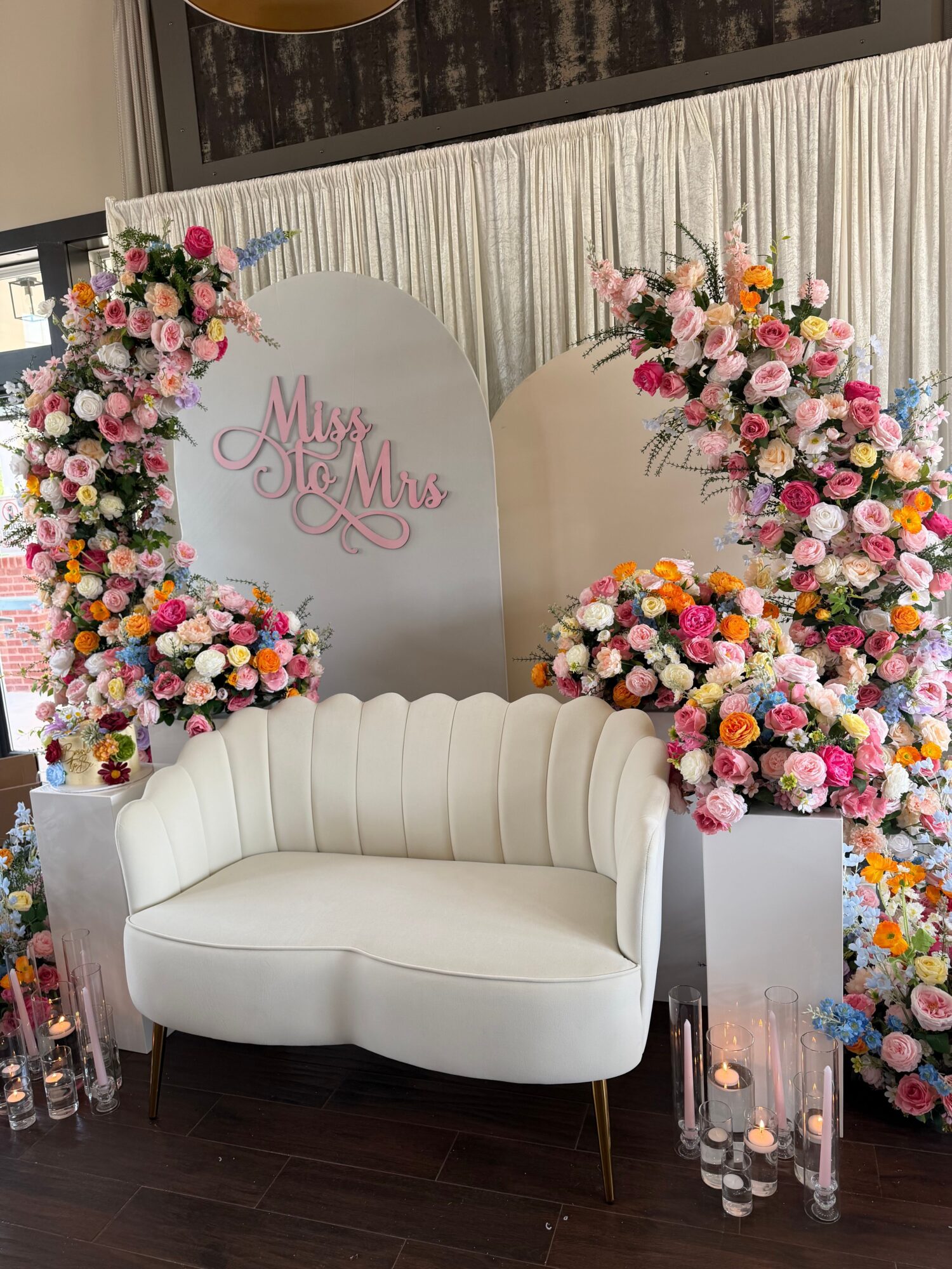 Decorative floral arrangement with pink, white, and yellow flowers, a white curved sofa, and a sign reading 'Mr. & Mrs.'