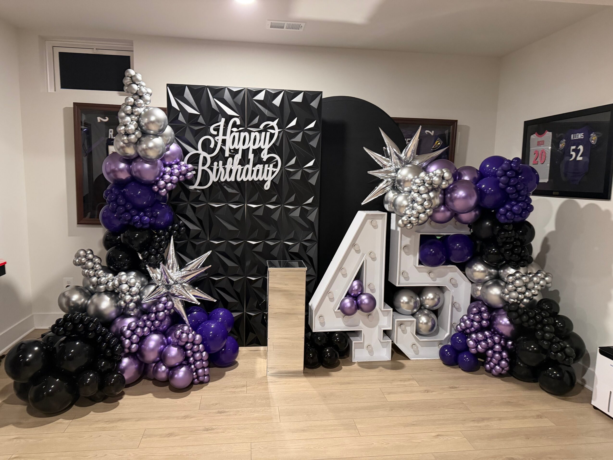 Balloon arrangement with silver, purple, and black balloons, large number 45, and a birthday sign, in a decorated room.