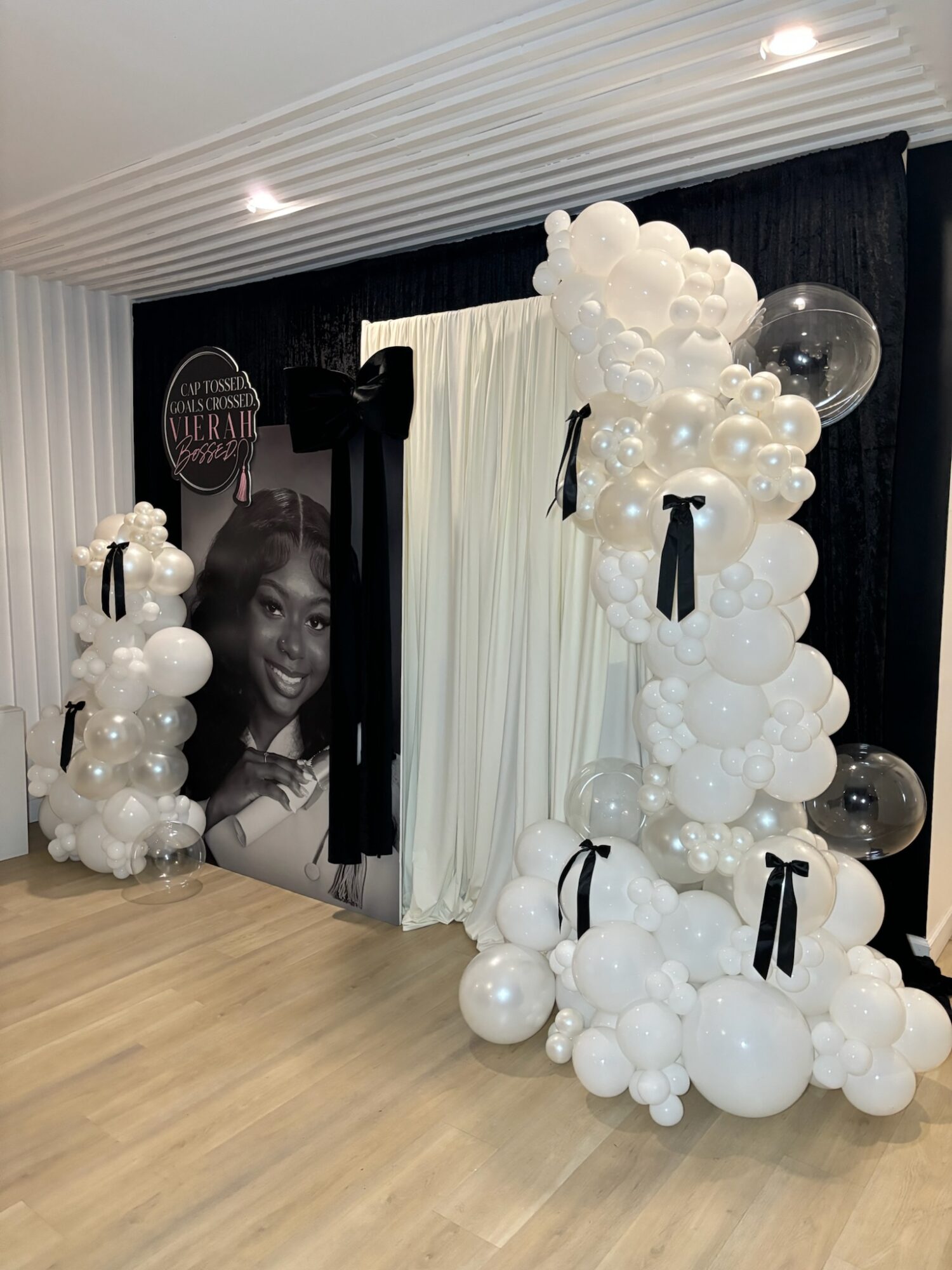 Decorative balloon arrangement with white and transparent balloons, black ribbons, and a black-and-white photo of a smiling woman in the background.