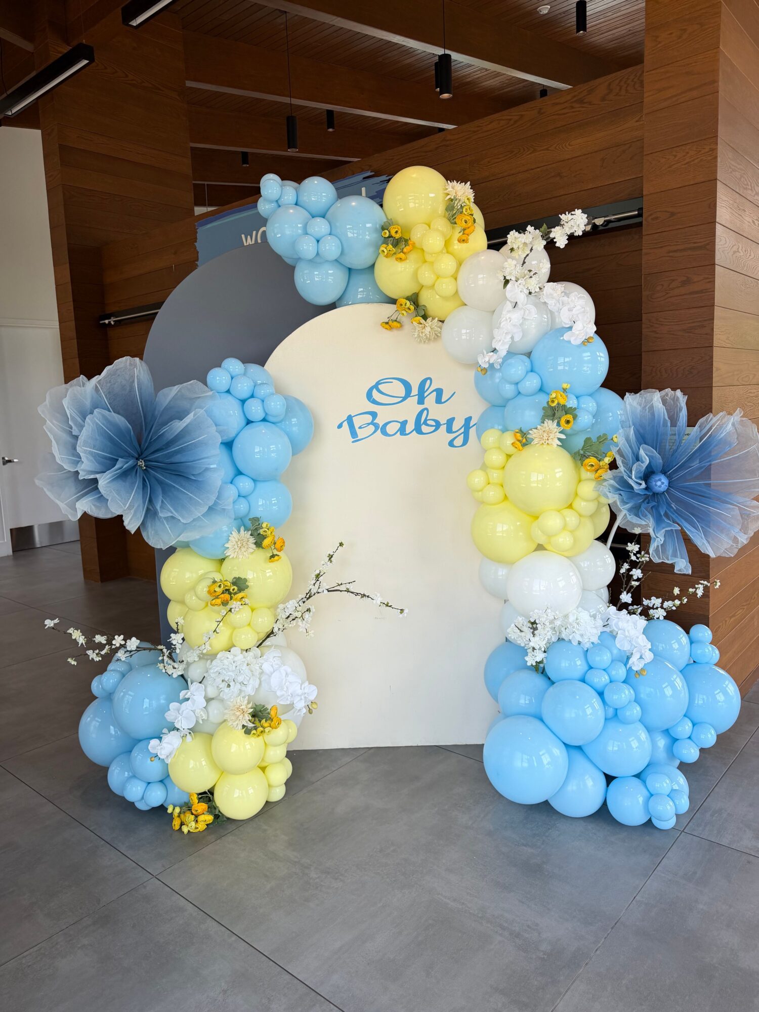 Decorative arrangement of blue, yellow, and white balloons with large blue paper flowers around a white board.
