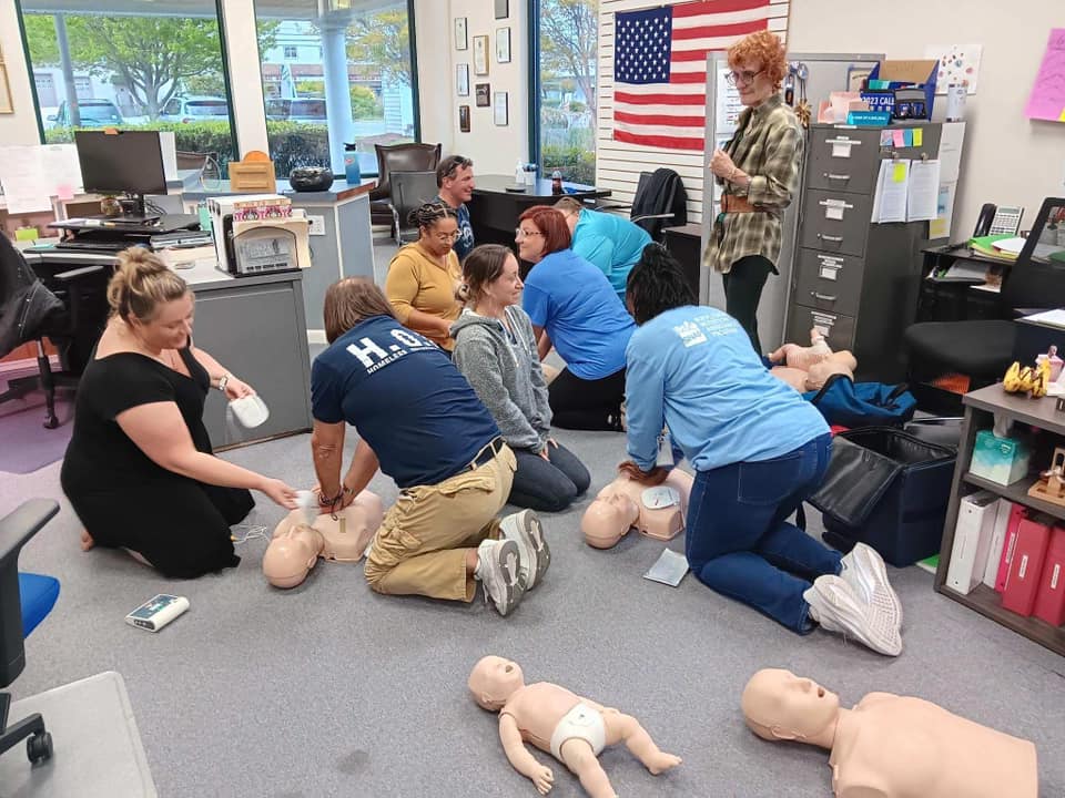 Group of people practicing CPR on mannequins in a classroom with an American flag on the wall.