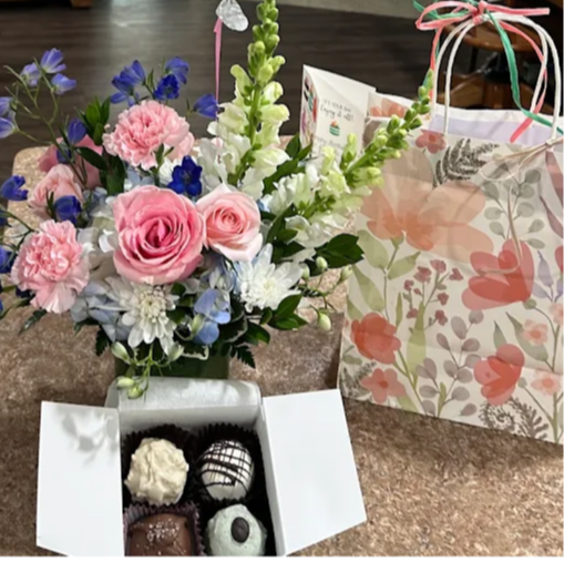 Colorful flower bouquet with pink roses, white and blue flowers, and a box of assorted chocolates on a table.