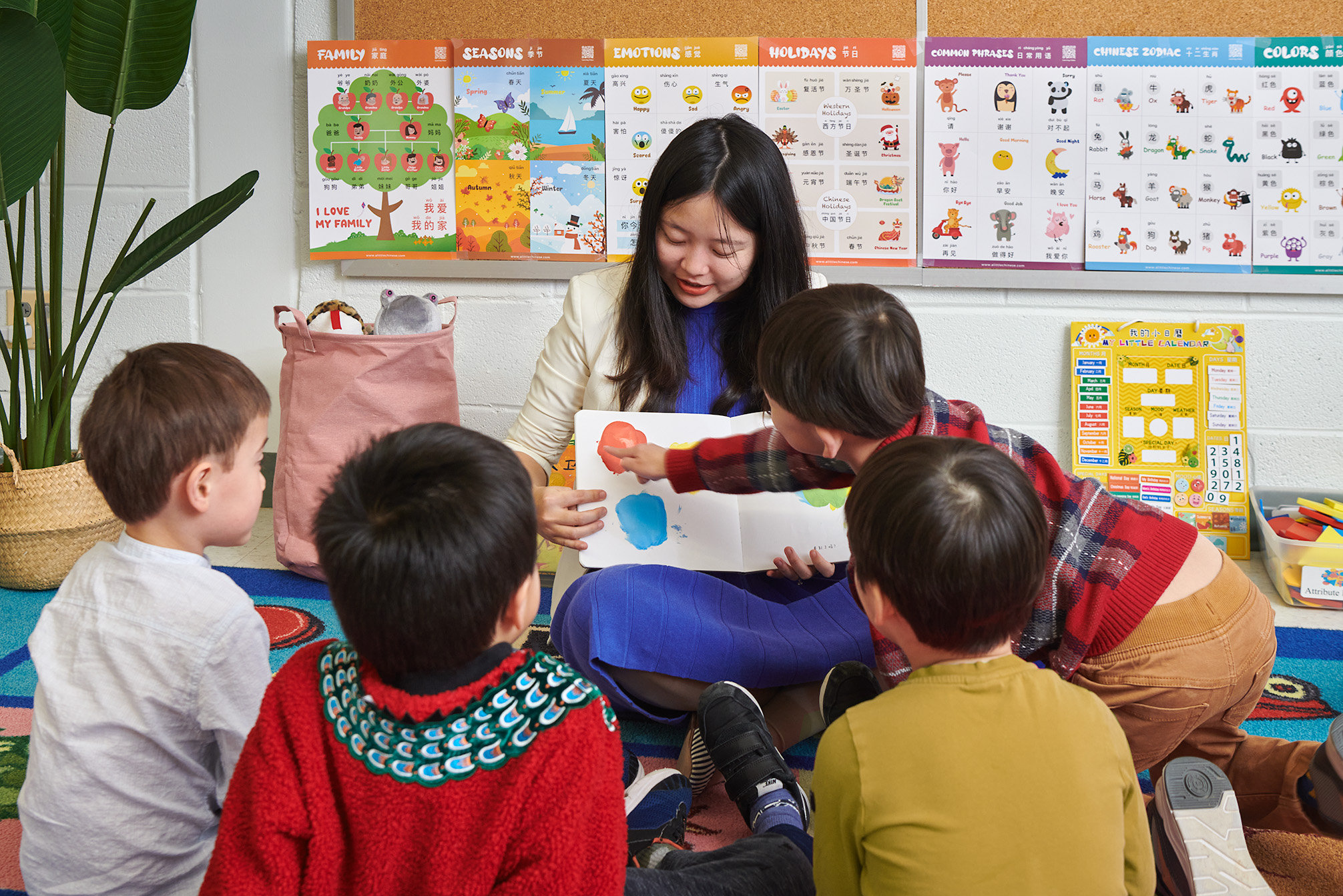 Teacher reading to four children in a classroom with colorful educational posters on the wall.