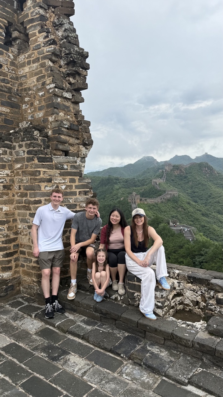 Four people sitting on a stone ledge near an ancient brick wall with mountains in the background.