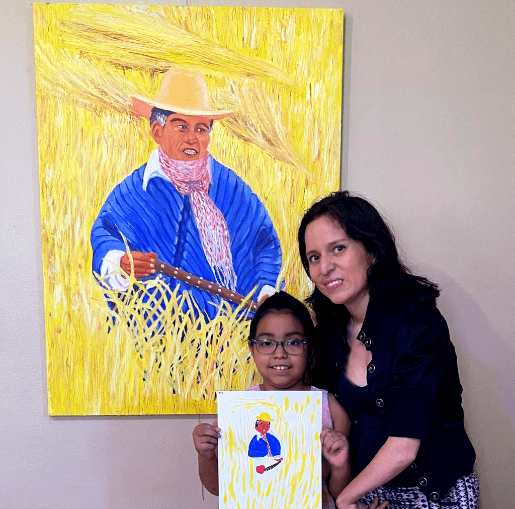 Woman and child holding a drawing in front of a colorful painting of a person in a blue shirt and straw hat, with yellow background.