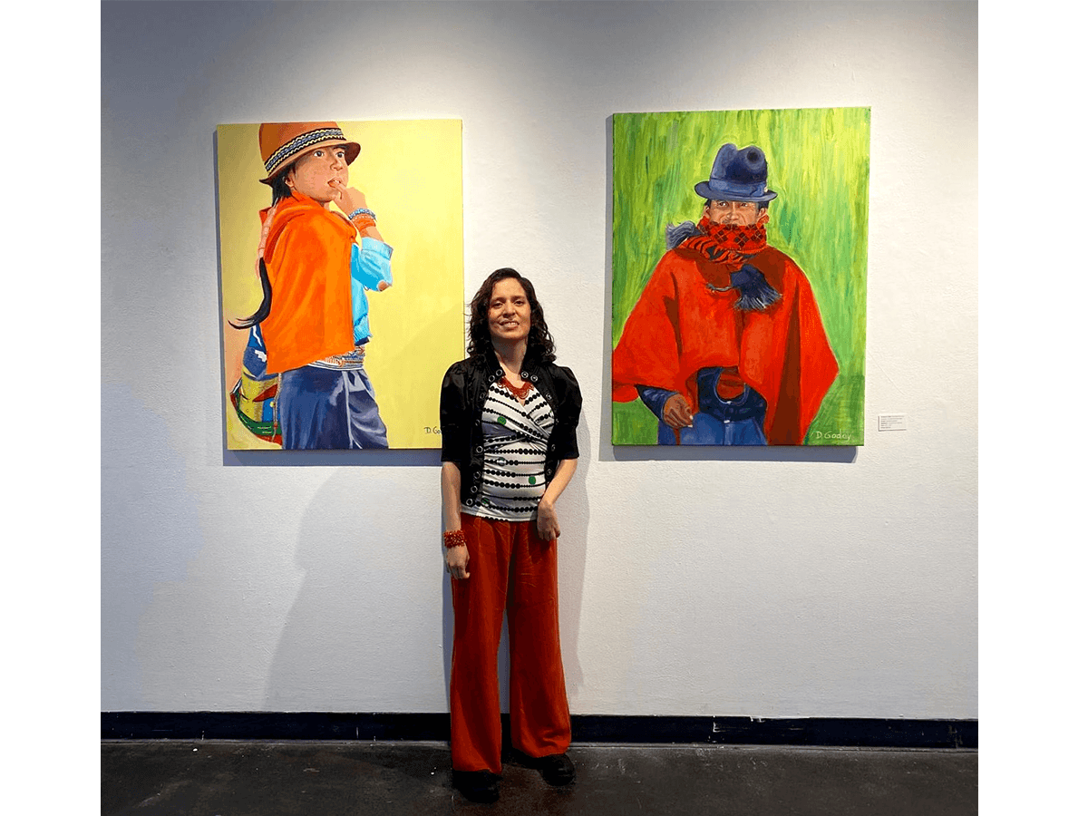 Woman standing in front of two colorful paintings of children wearing hats and coats, gallery setting.