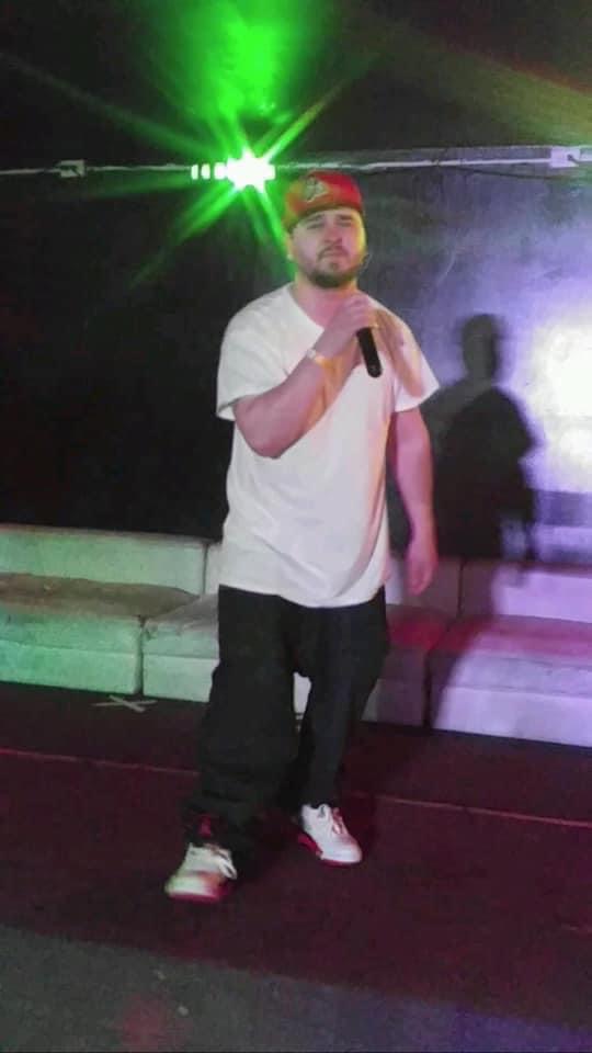 Man holding microphone on stage with colorful lights and shadow in background.