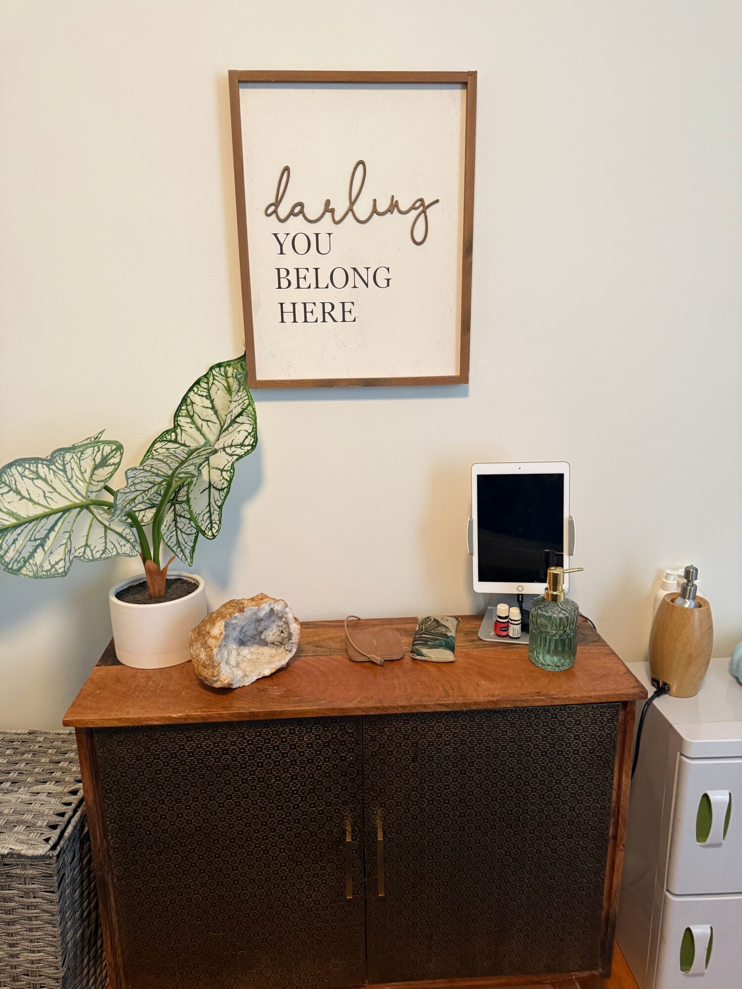 Wooden cabinet with decorative items, a potted plant, and a framed quote on a wall, viewed from the side.