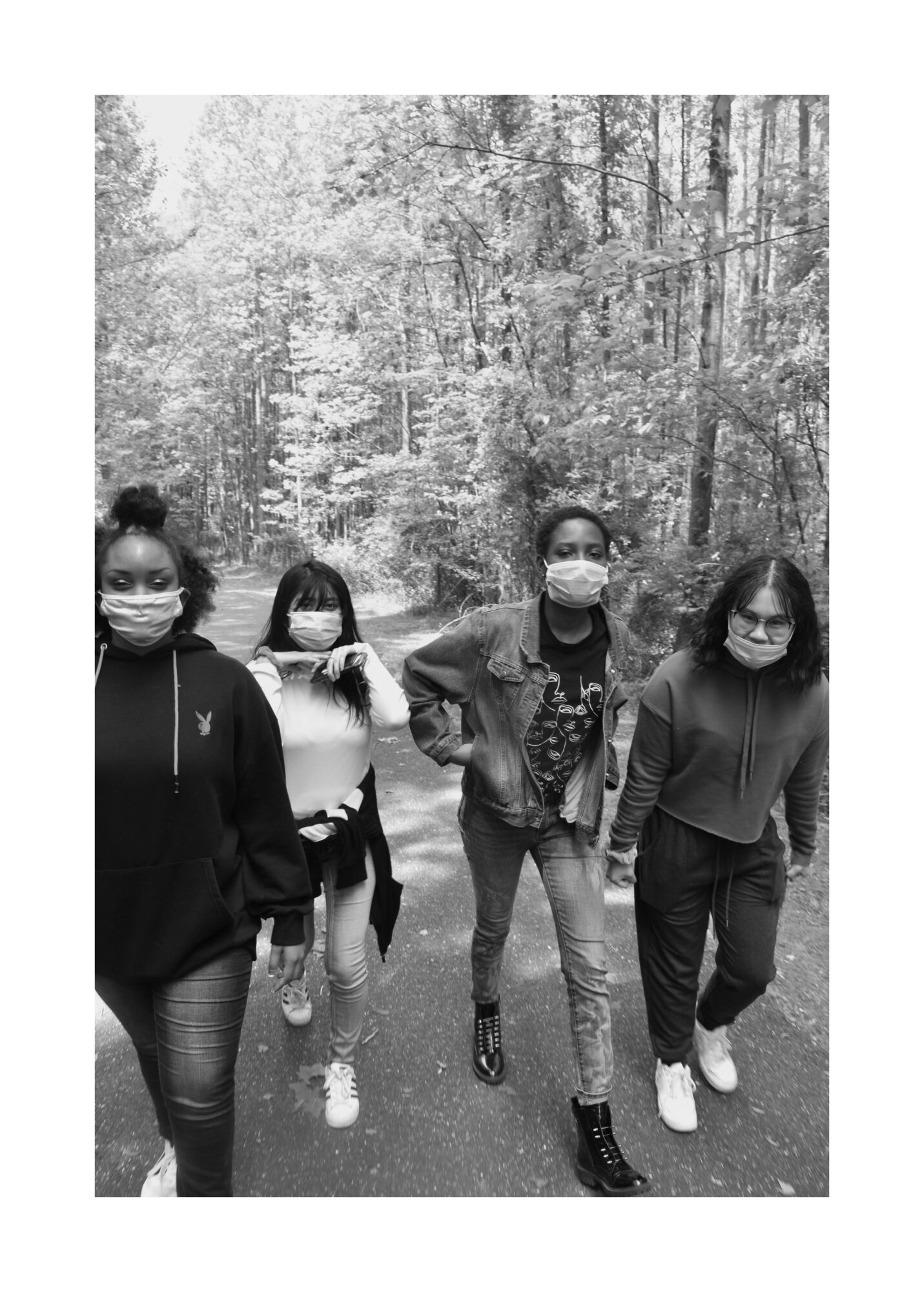 Four people walking on a forest path, all wearing face masks, trees in the background.
