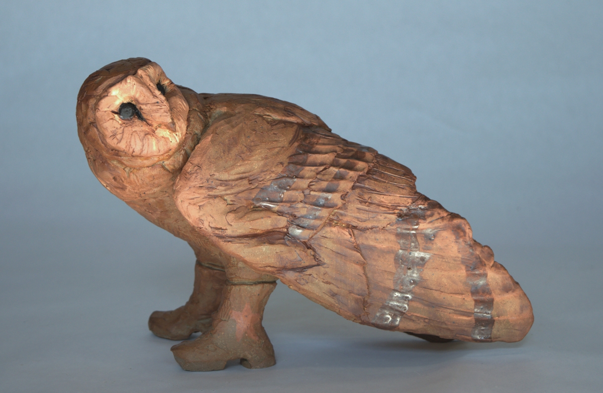 Clay sculpture of an owl with a rounded head, perched on a base, with detailed feathers and textured surface.