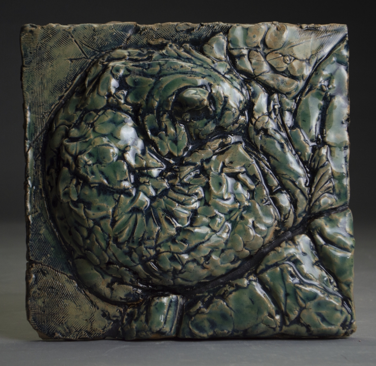 A textured, greenish metallic sculpture of a curled-up animal, possibly a turtle, with detailed shell and limbs.