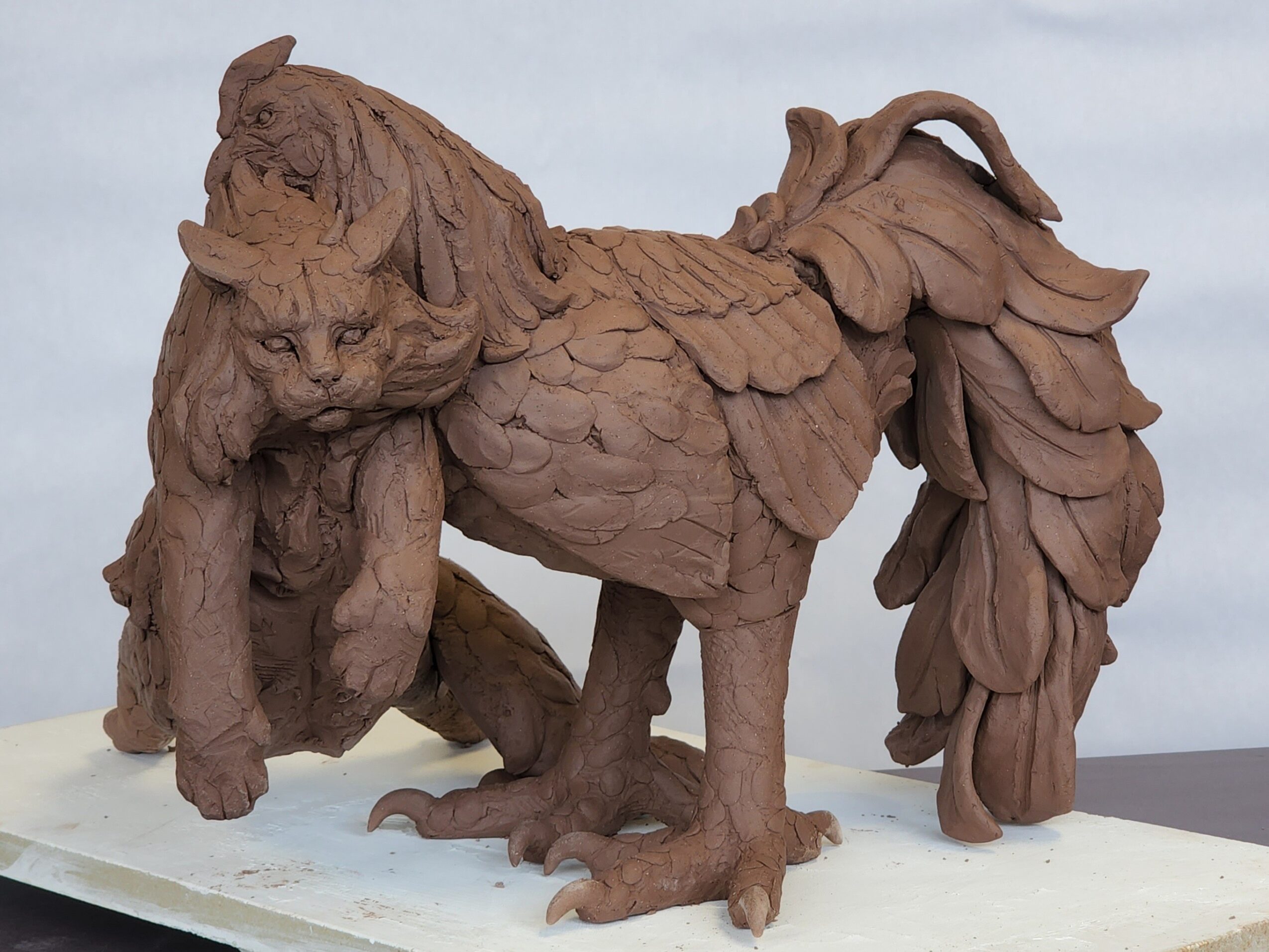 Wooden sculpture of a creature with the body of a lion and the head of a dog, standing on a white base.