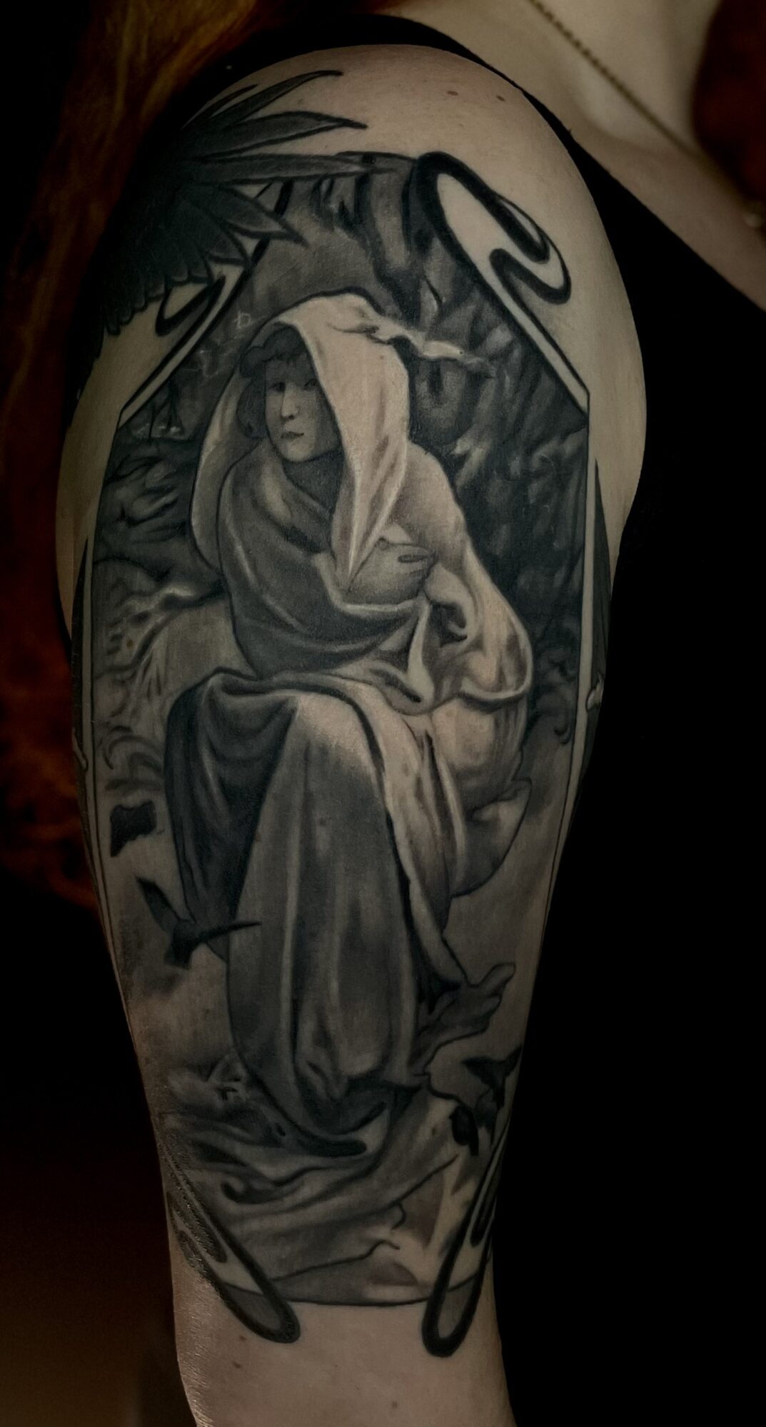 Tattoo of a woman with a hood sitting among trees and foliage, in black and gray shading.