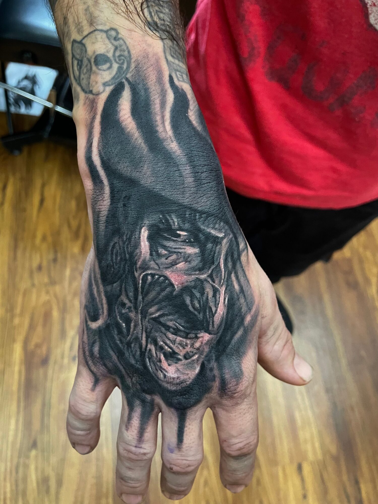 Tattooed hand with a detailed black and gray dog portrait and a small bear face on the wrist.