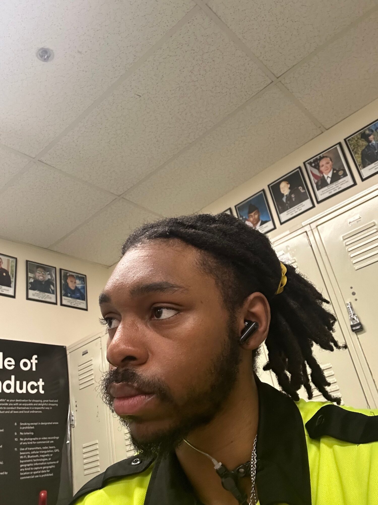 Person with dreadlocks looking to the side in an indoor setting, with photos and lockers in the background.