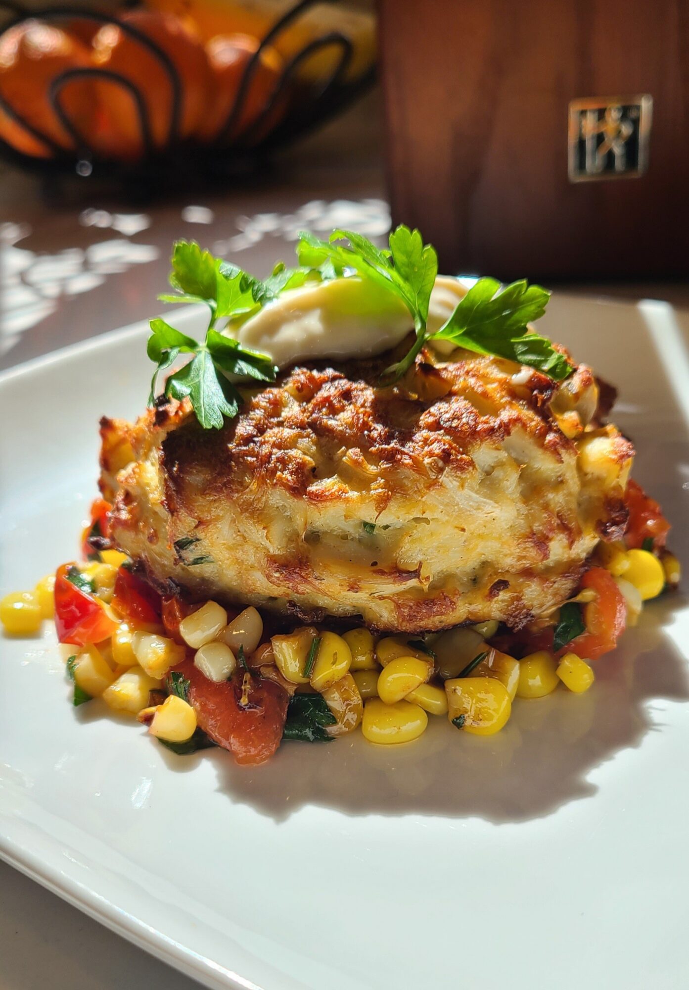 A slice of casserole with a meat topping, served on a white plate with corn and vegetables, garnished with parsley and a dollop of sour cream.