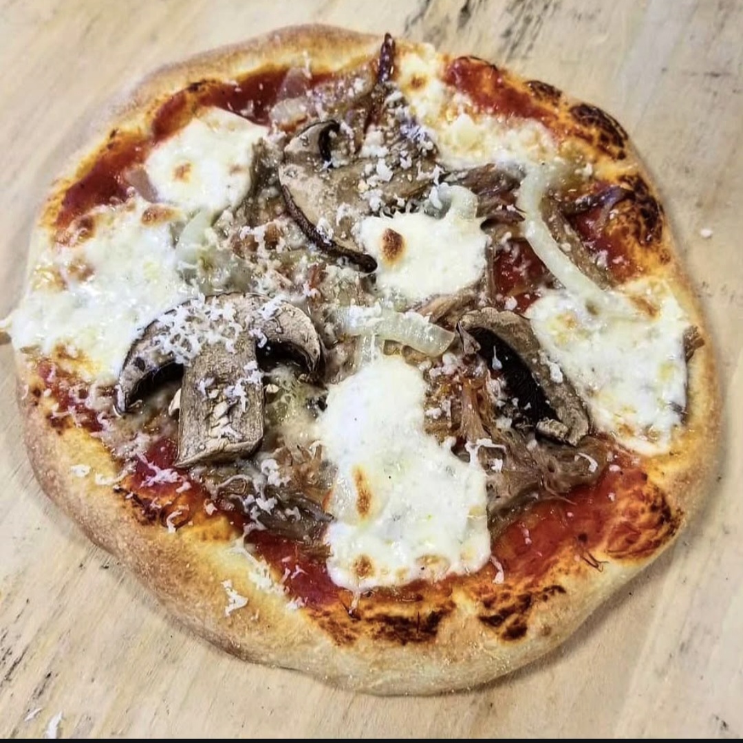 Pizza with cheese, mushrooms, and grated cheese on a wooden surface.