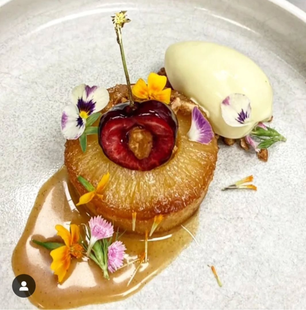 Dessert with a caramelized fruit, edible flowers, and a scoop of ice cream on a plate.
