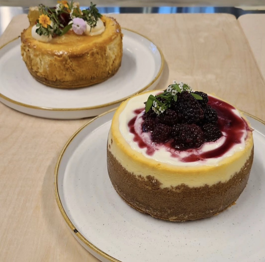Two desserts on plates, one with flowers and the other with berries and sauce, on a wooden table.