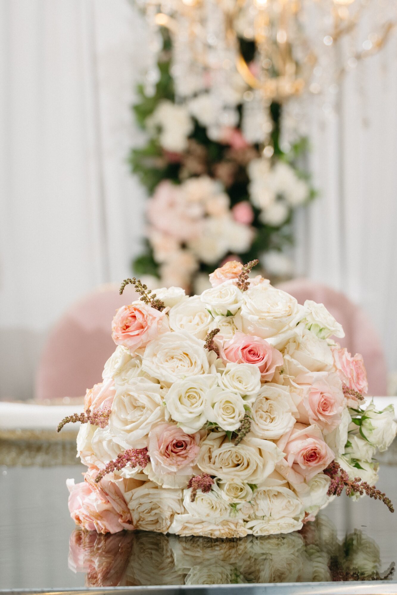 Close-up of a bouquet of white and pink roses on a reflective surface, with a blurred floral arrangement in the background.