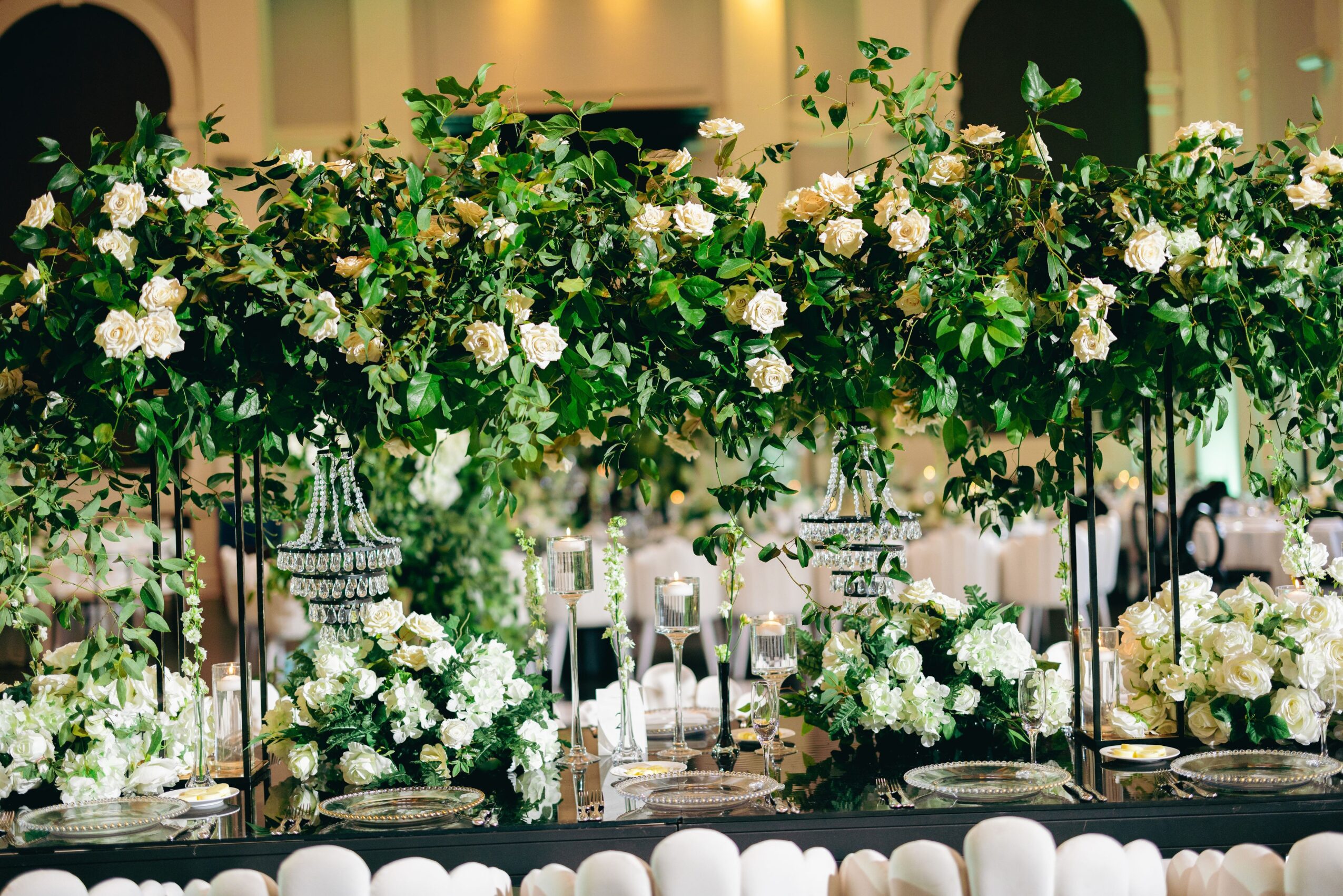 Elegant table decorated with white flowers and greenery, with tall floral arrangements and candles, in a formal event setting.