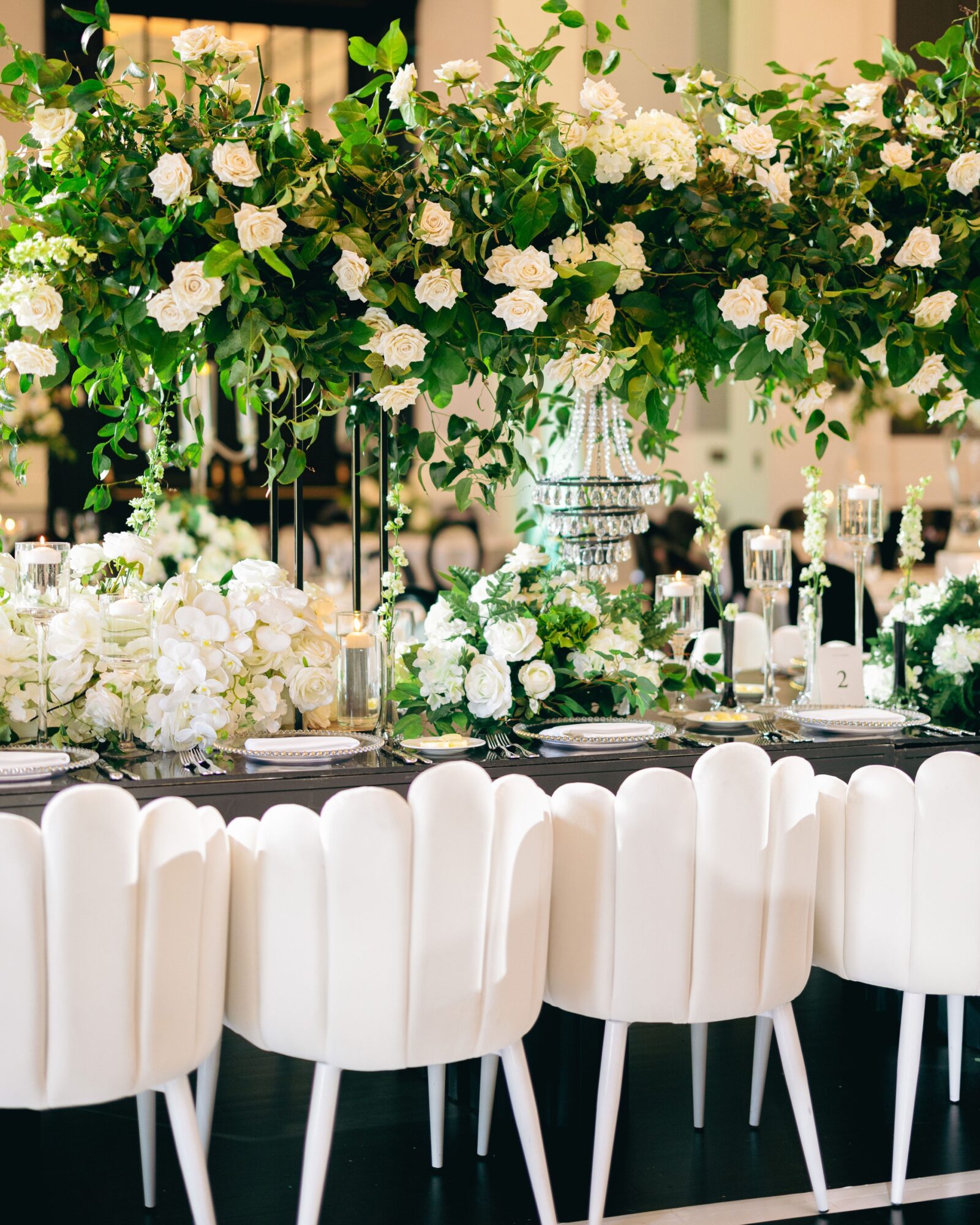 Elegant table setting with white chairs and a large floral centerpiece of white and green flowers.