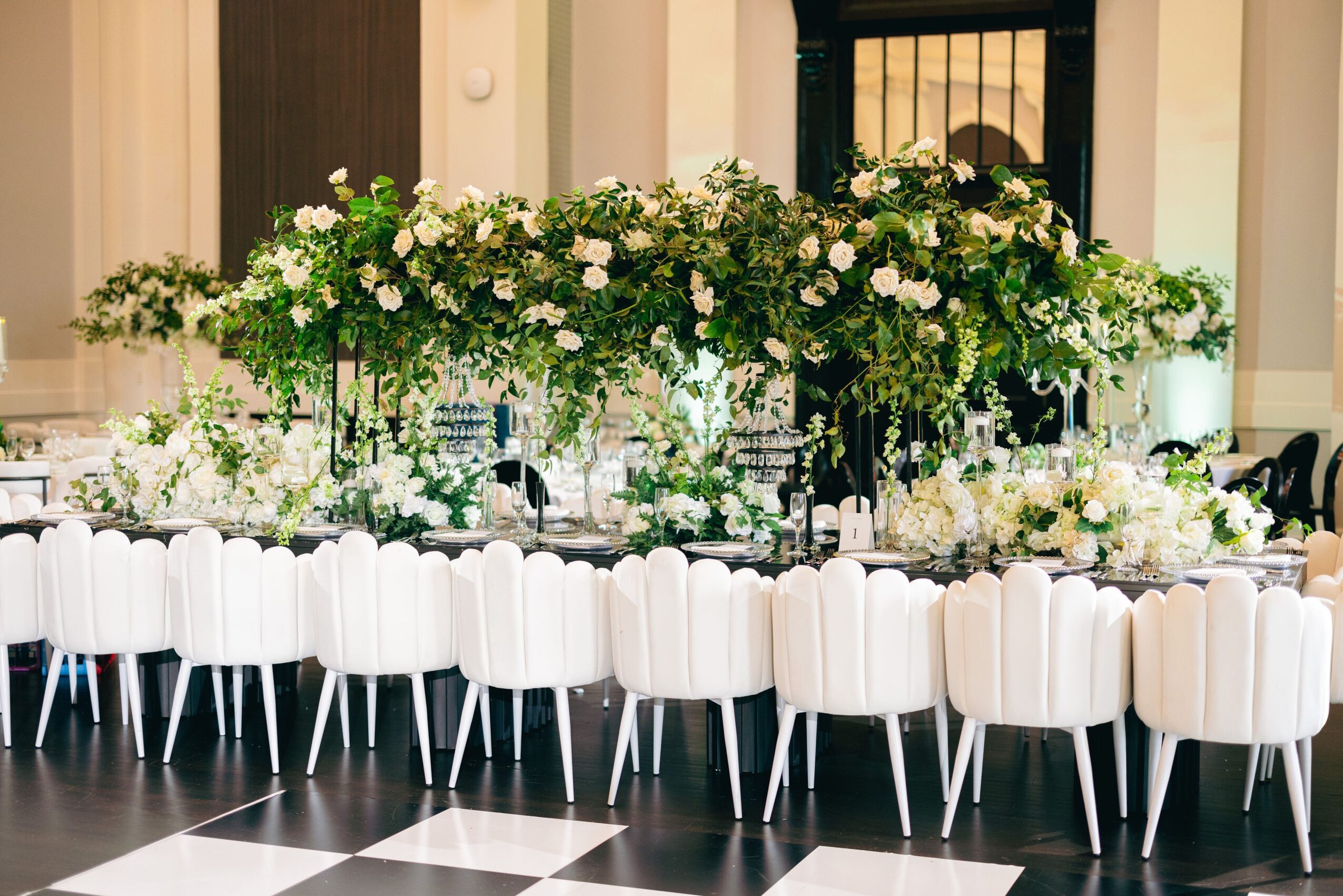Elegant table setup with white chairs and a lush floral centerpiece in a bright room.