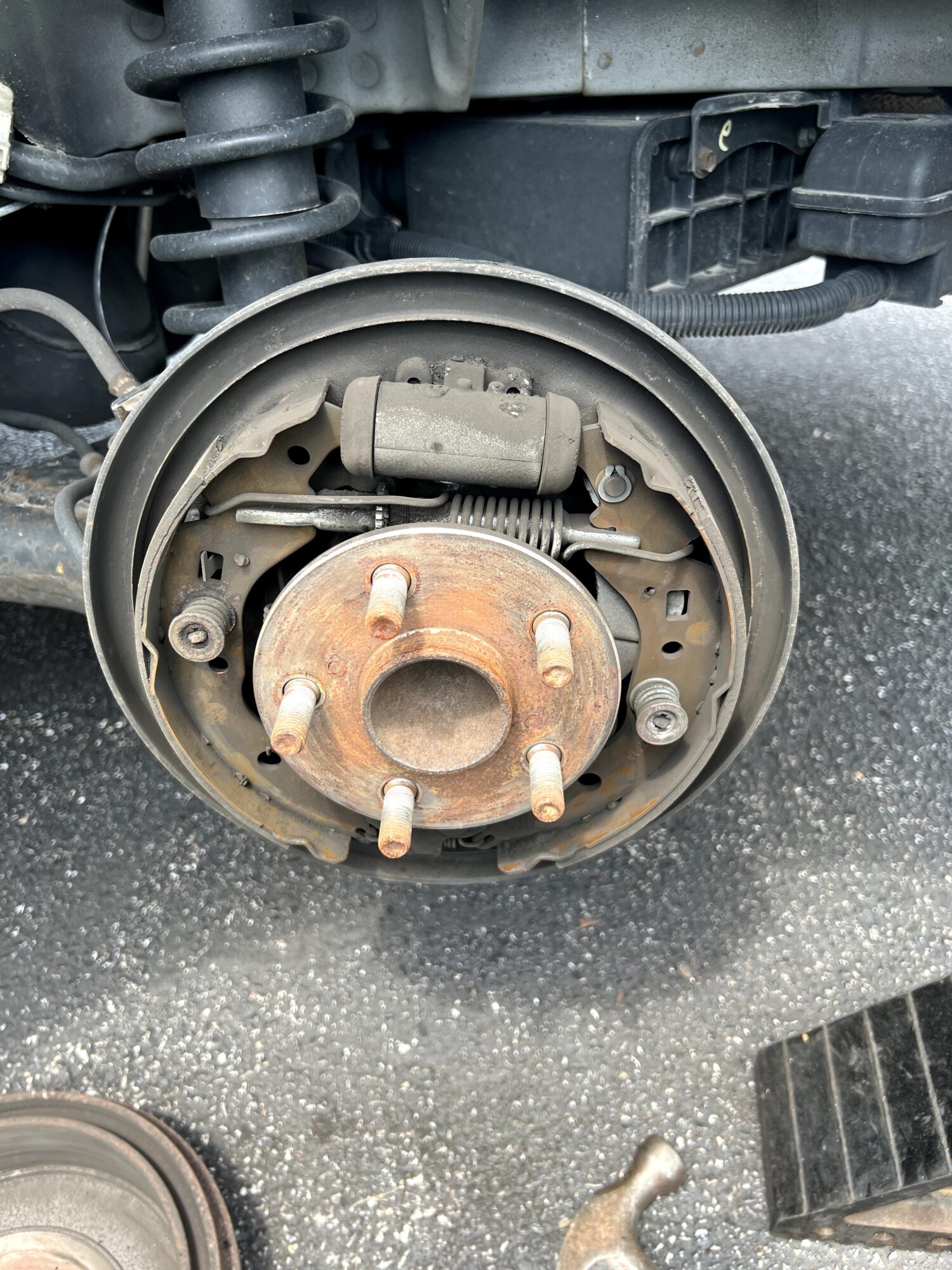 Car wheel hub with brake drum removed, showing brake shoes and suspension components, on asphalt surface.