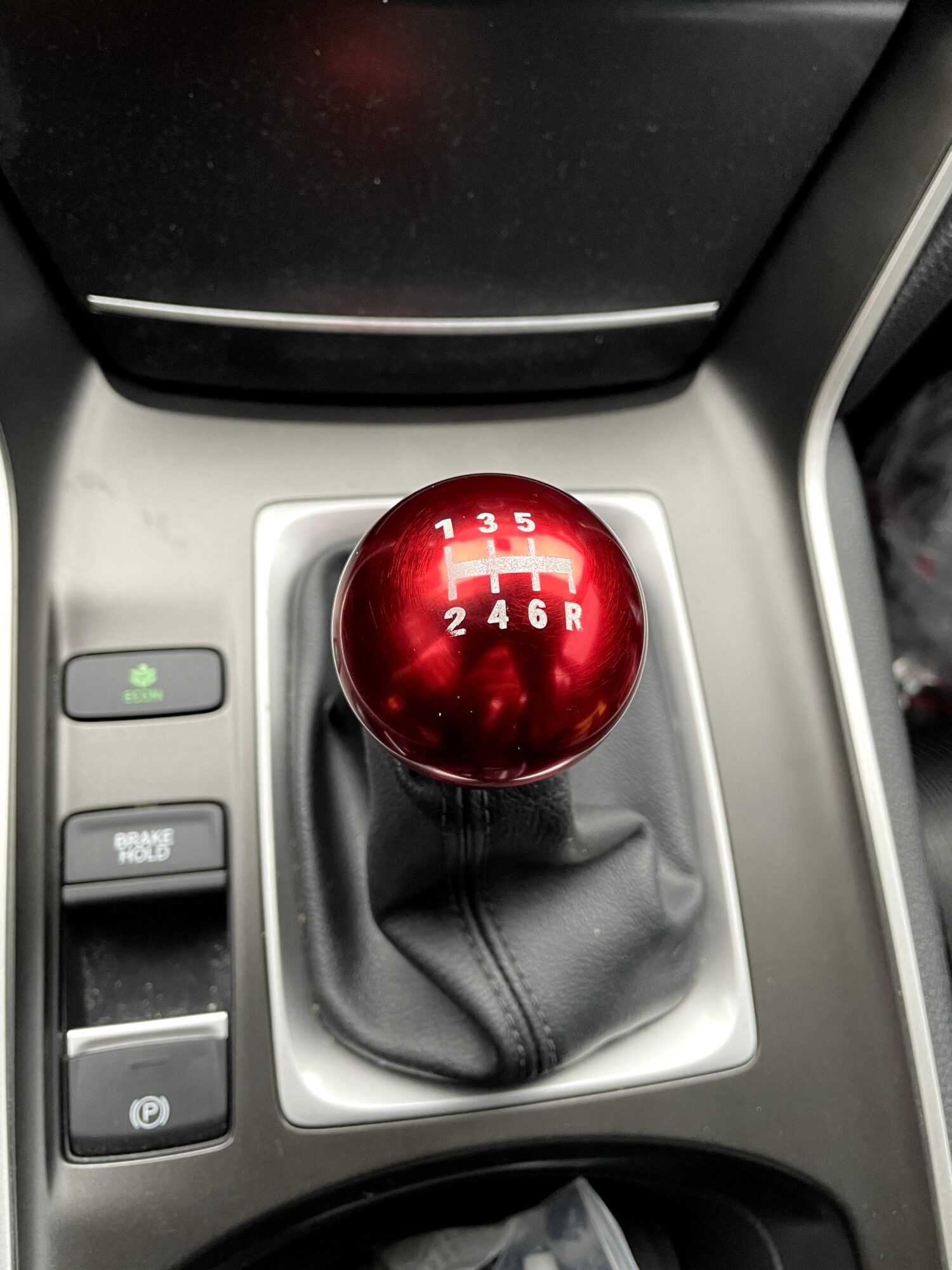 Red gear shift knob with six-speed pattern in a car interior, surrounded by buttons and console.